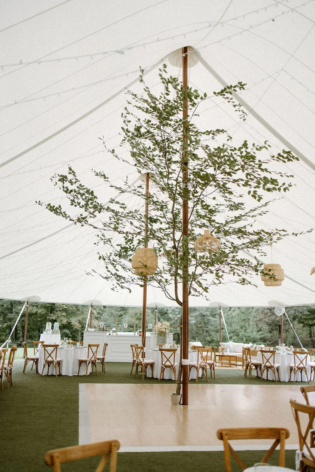 White sailcloth wedding tent with natural wooden furnishings and surrounding garden greenery.