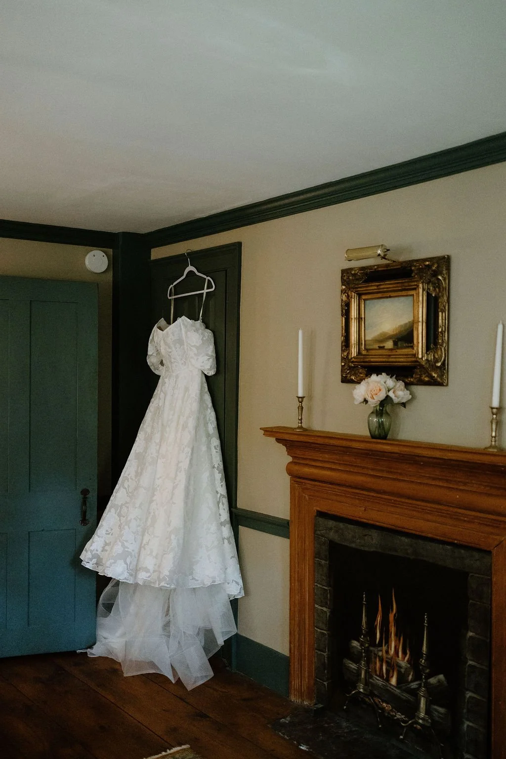 White bridal gown hanging beside a fireplace in the elegant estate getting-ready room.