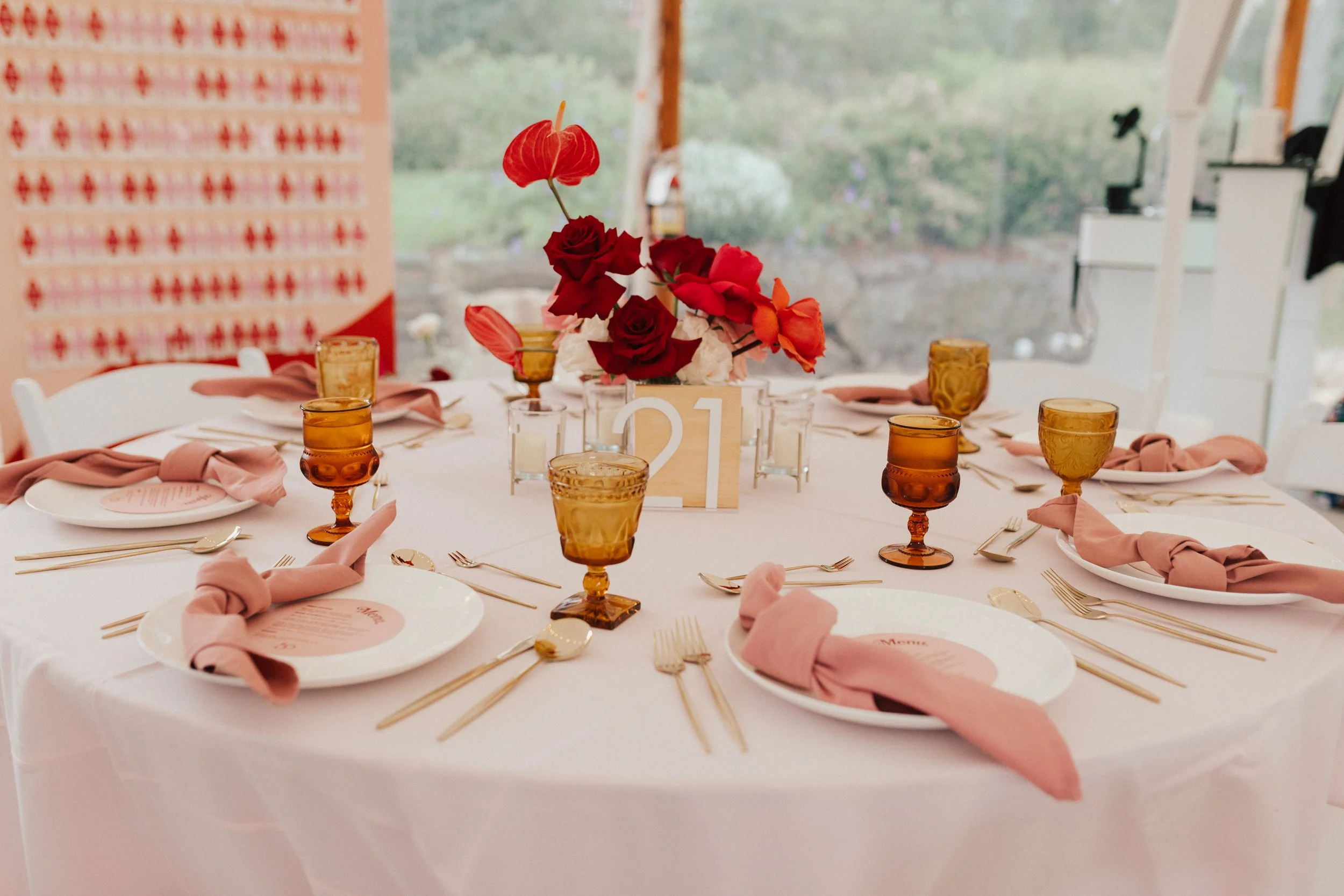 Vibrant wedding centerpiece with coral, pink, and red roses paired with modern anthuriums and glass votives.