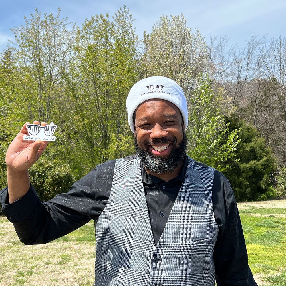 Man wearing a vest and an Evan Doan Jenkions logo hat and holding an Evan Doan Jenkins sticker