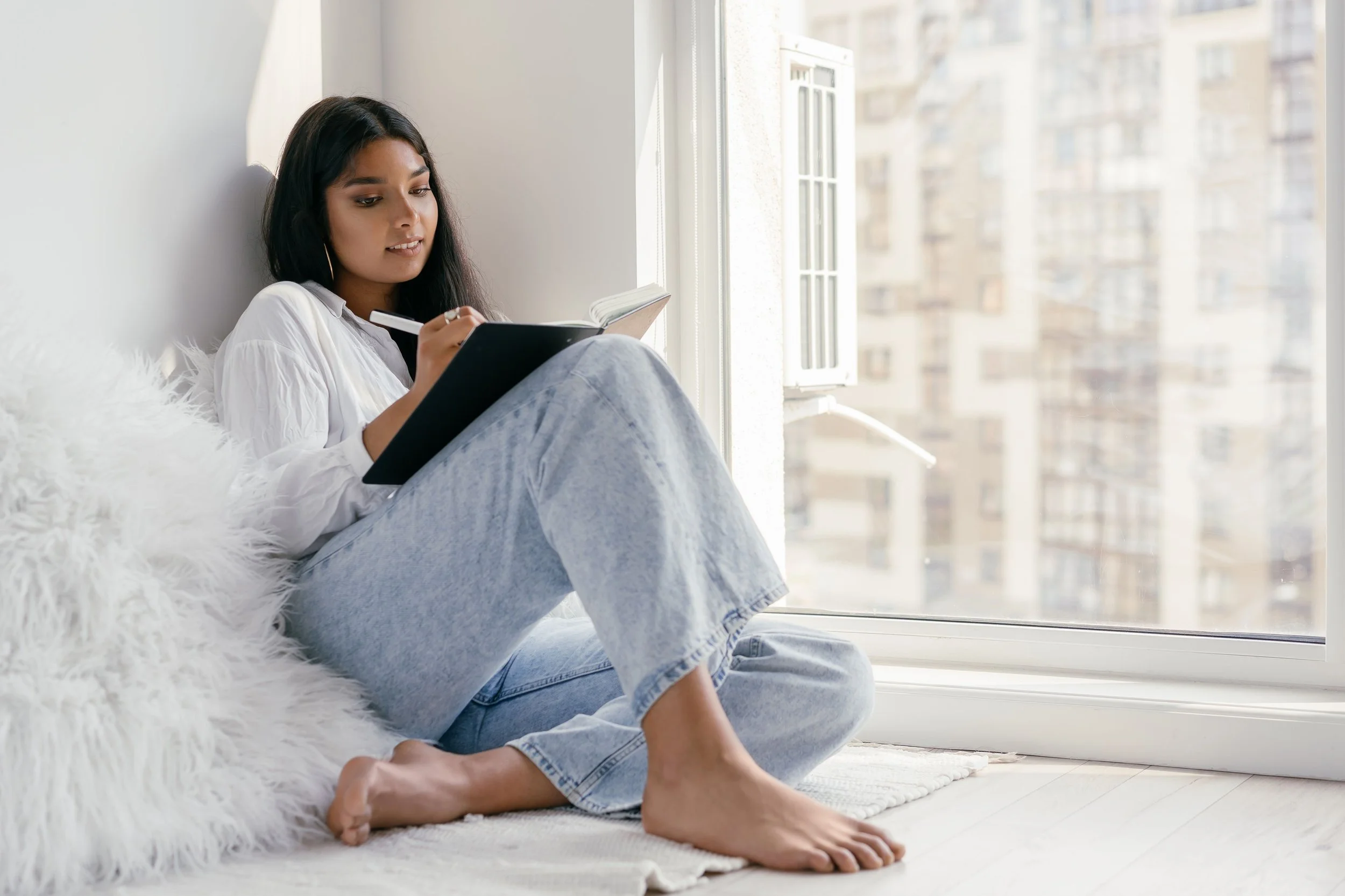 black woman sitting with a journal, writing, sitting by a window