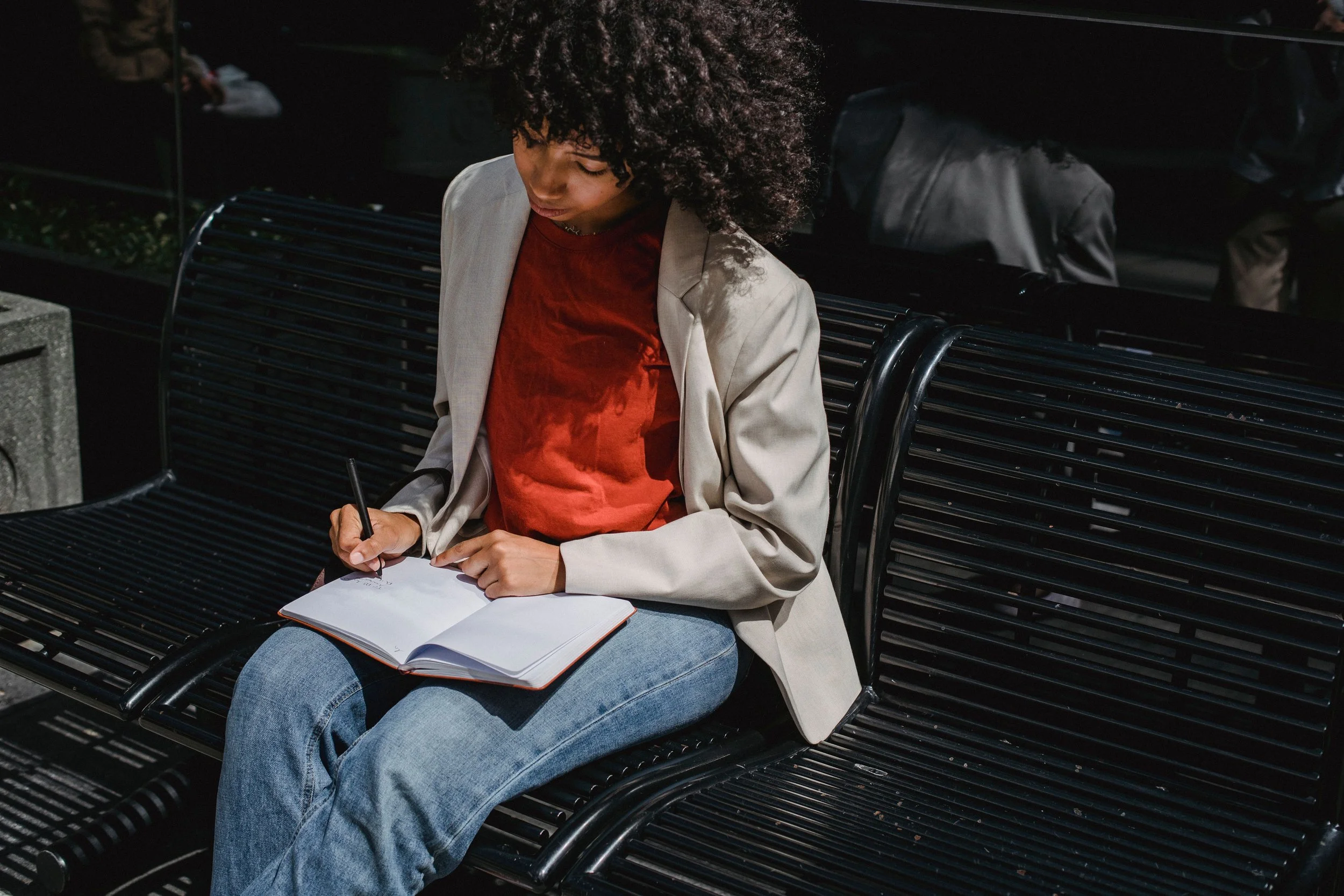 black woman sitting alone on bench journaling
