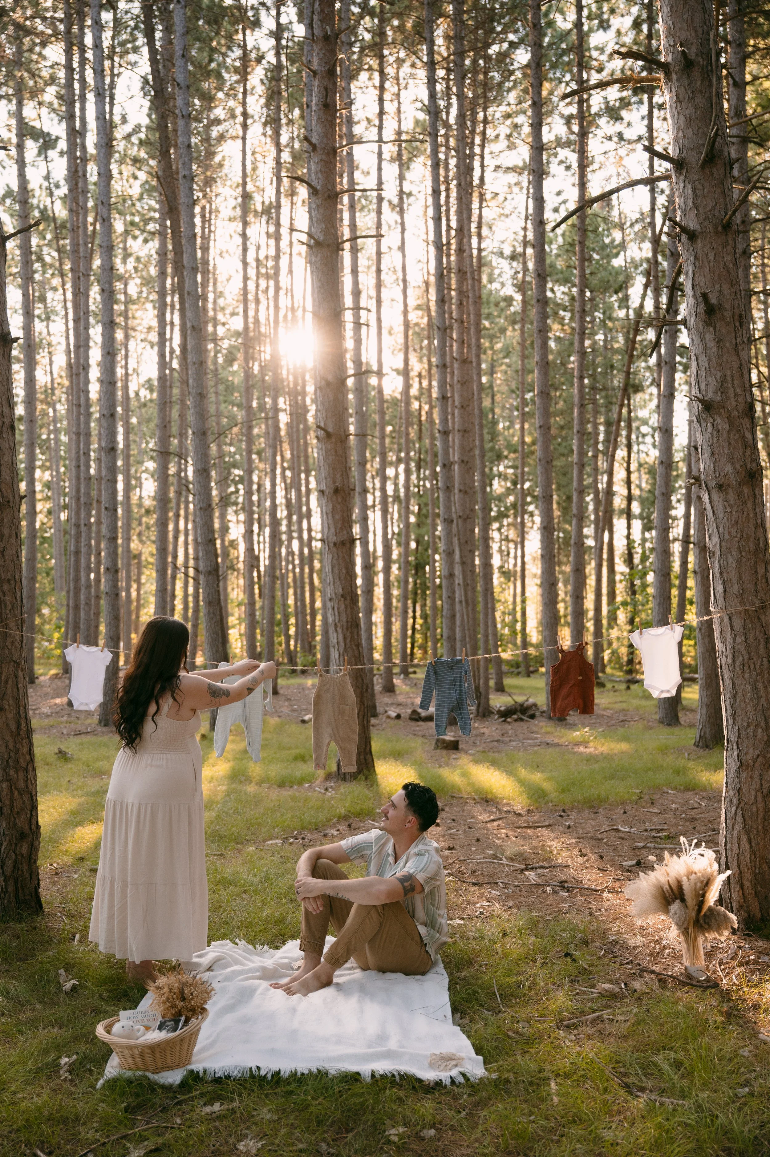 a maternity photo where the mother is hanging baby clothes on a clothesline while the father admires his wife.