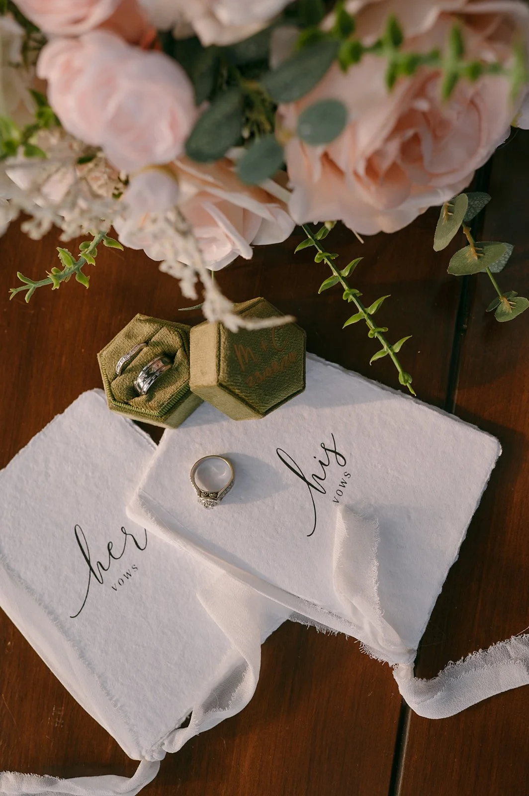 Wedding rings, flowers, and vows on a wooden surface.