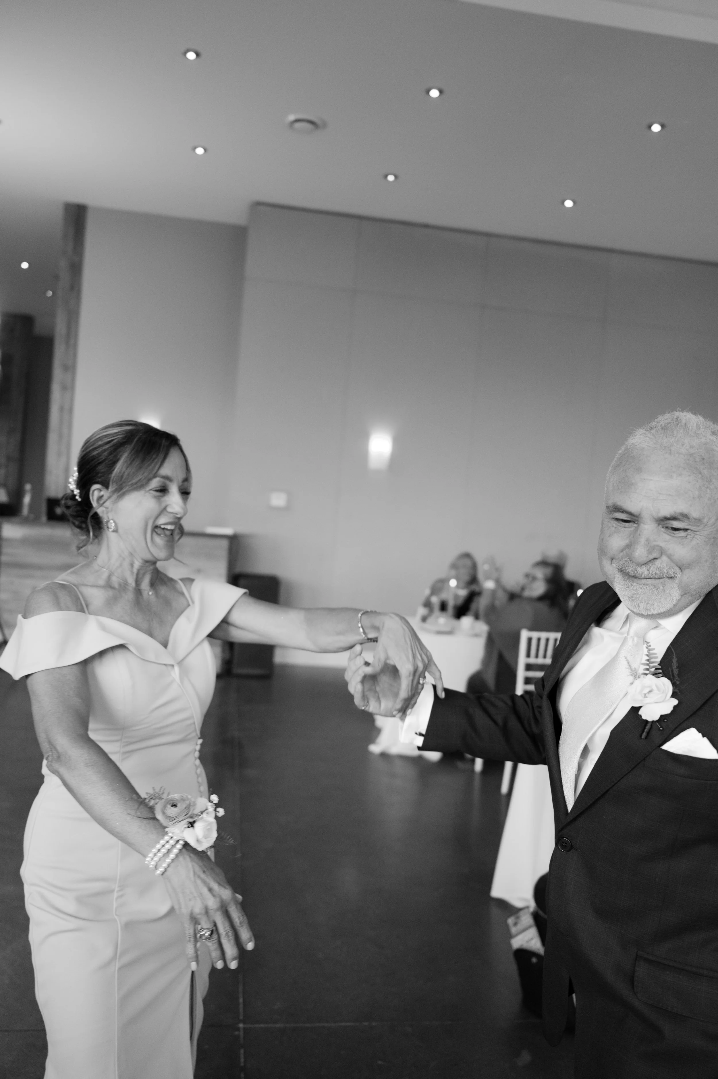 A joyful woman and an elderly man dancing together at a formal event, both dressed in elegant attire, with the woman in a light-colored gown and the man in a dark suit and tie.