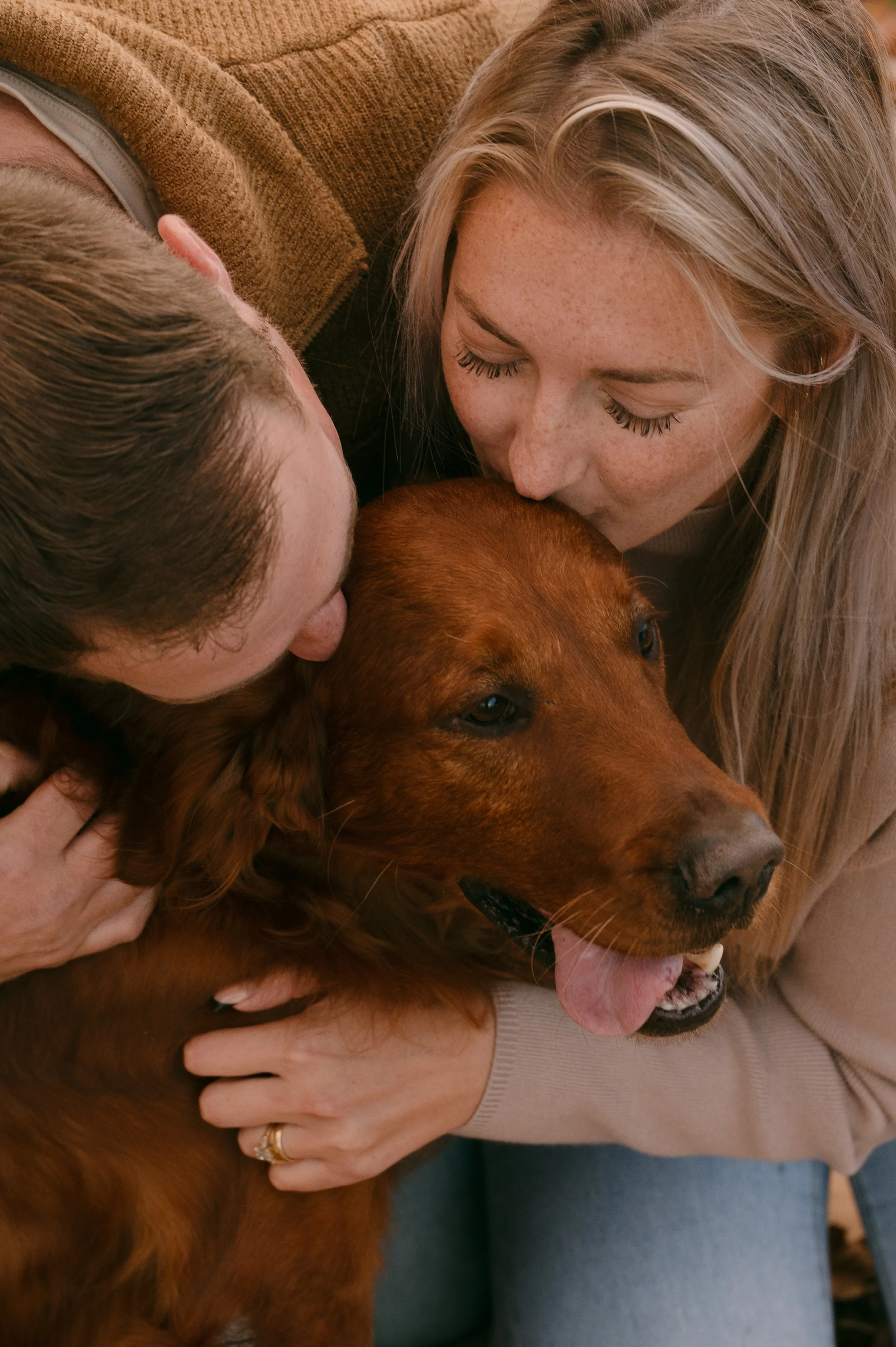 A woman and a man hugging a golden retriever dog.