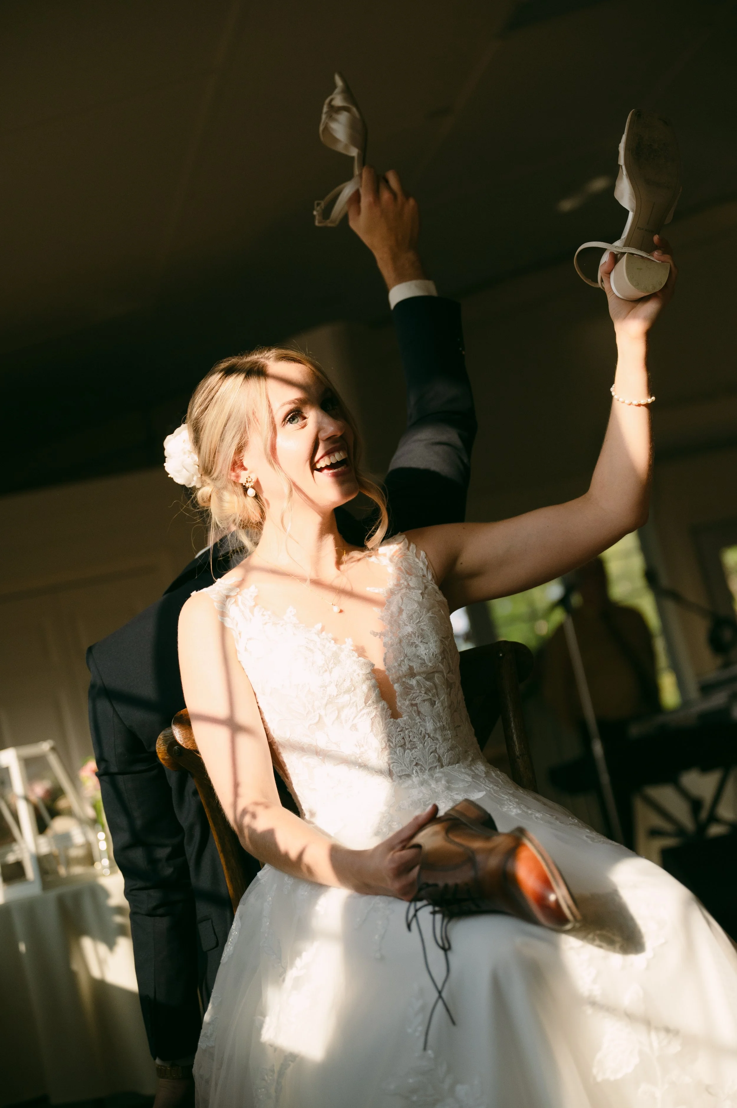 Happy bride in wedding dress holding a shoe and smiling at wedding reception.