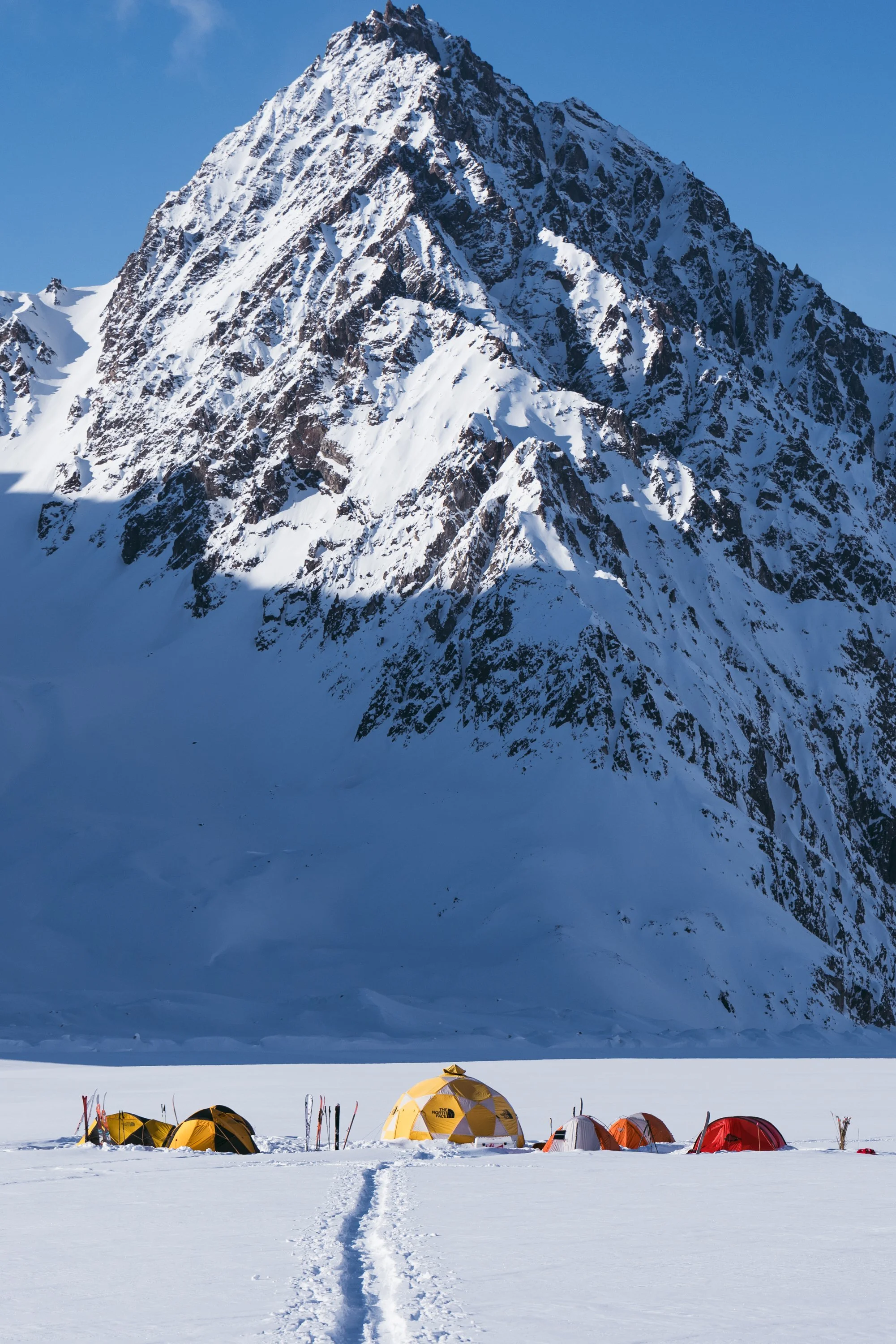 Multiple tents set up on snow with a large snow-covered mountain in the background.