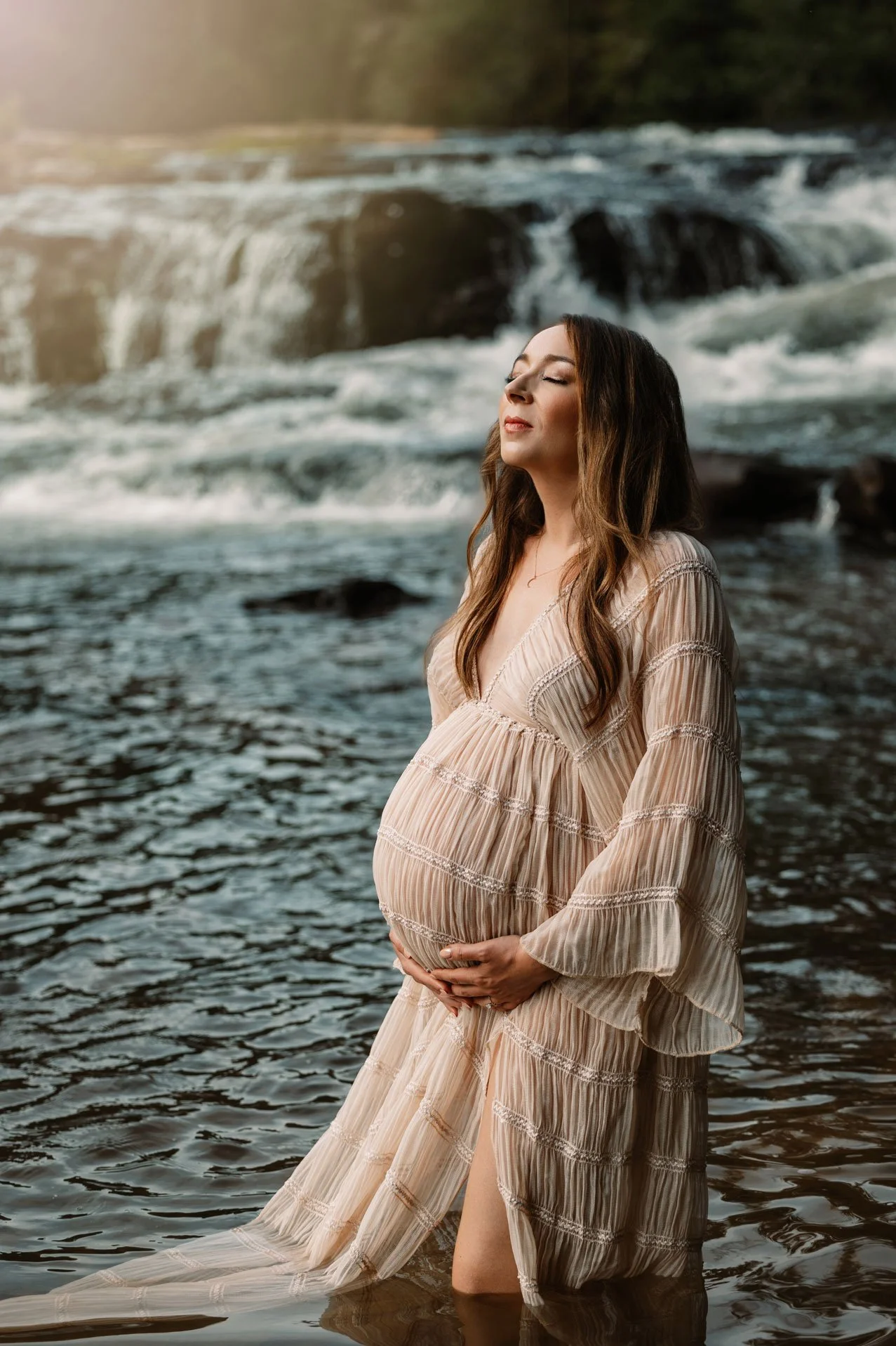 Pregnant woman standing knee-deep in a calm North Georgia creek, looking peaceful during her natural Dahlonega maternity photography session.