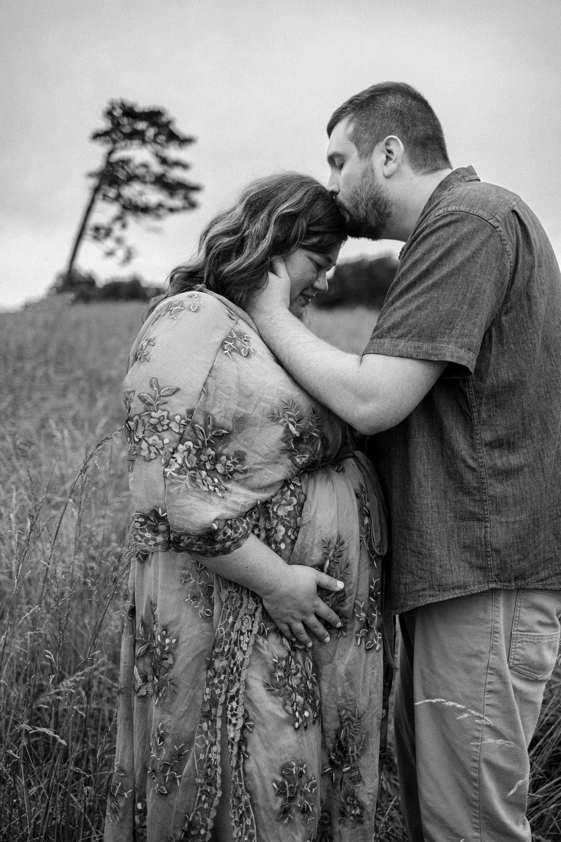 Expecting couple embracing in a grassy Dahlonega field during a maternity photo session with mountain views in the background