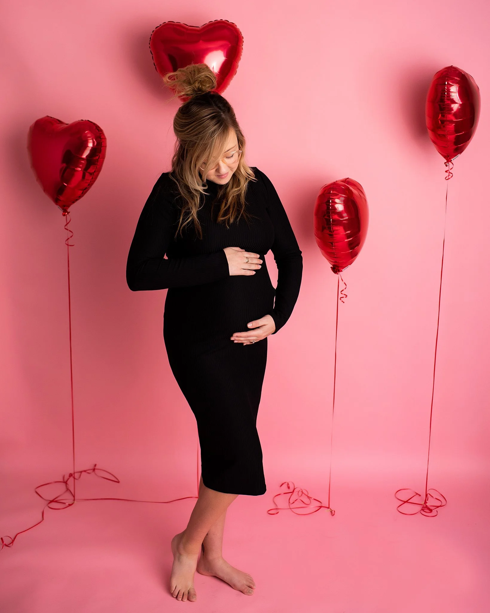 black maternity dress pregnant girl in front of pink backdrop and red balloons