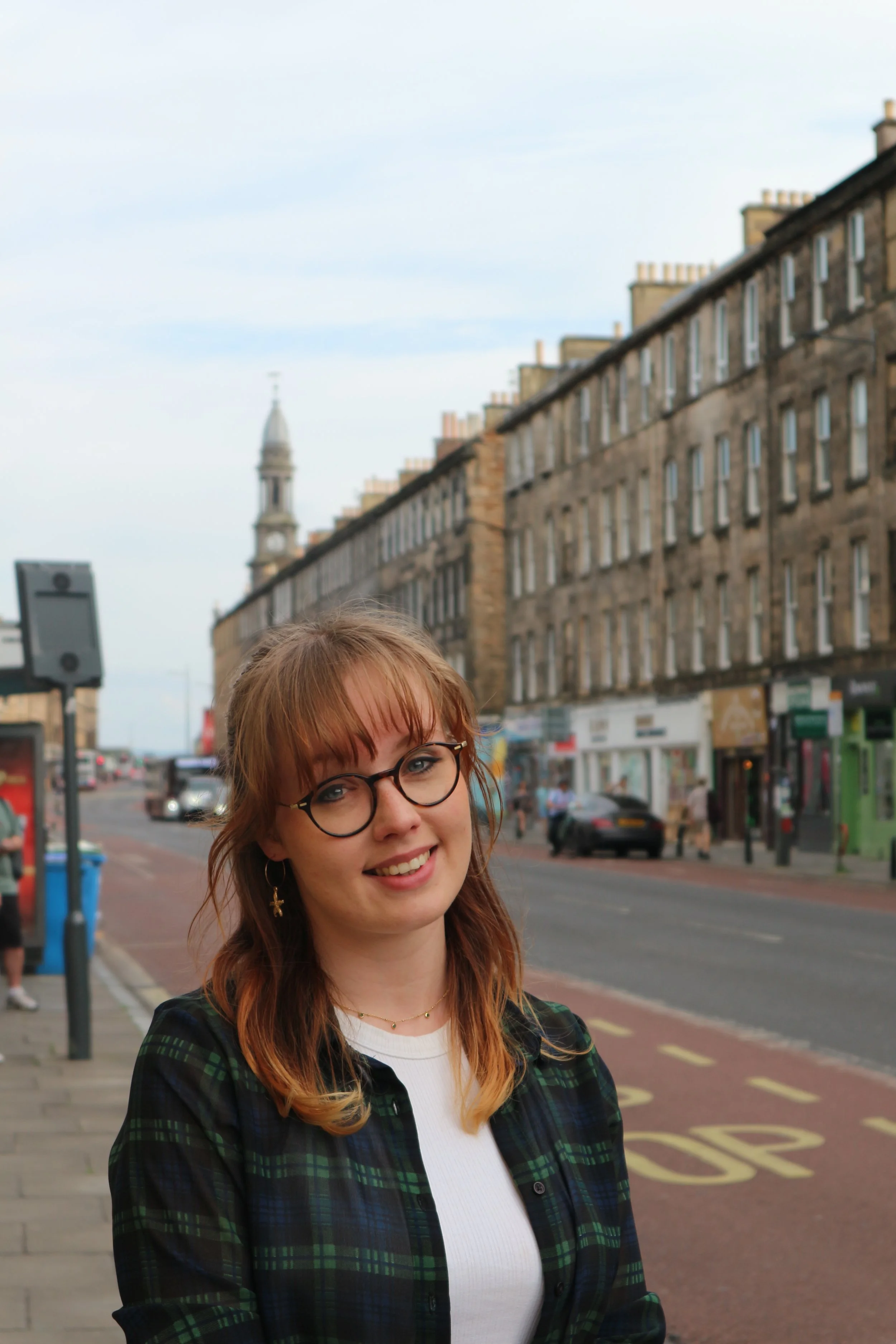 Portrait photo of Ruth Elliott smiling at the camera whilst standing on Clerk Street looking towards Queen's Hall