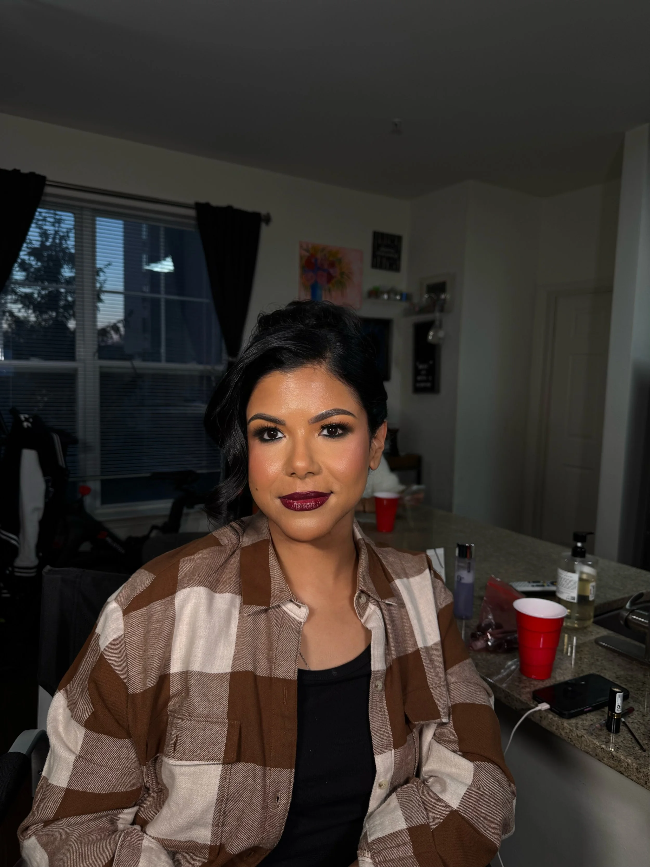 A woman with dark hair and makeup sitting at a kitchen counter.