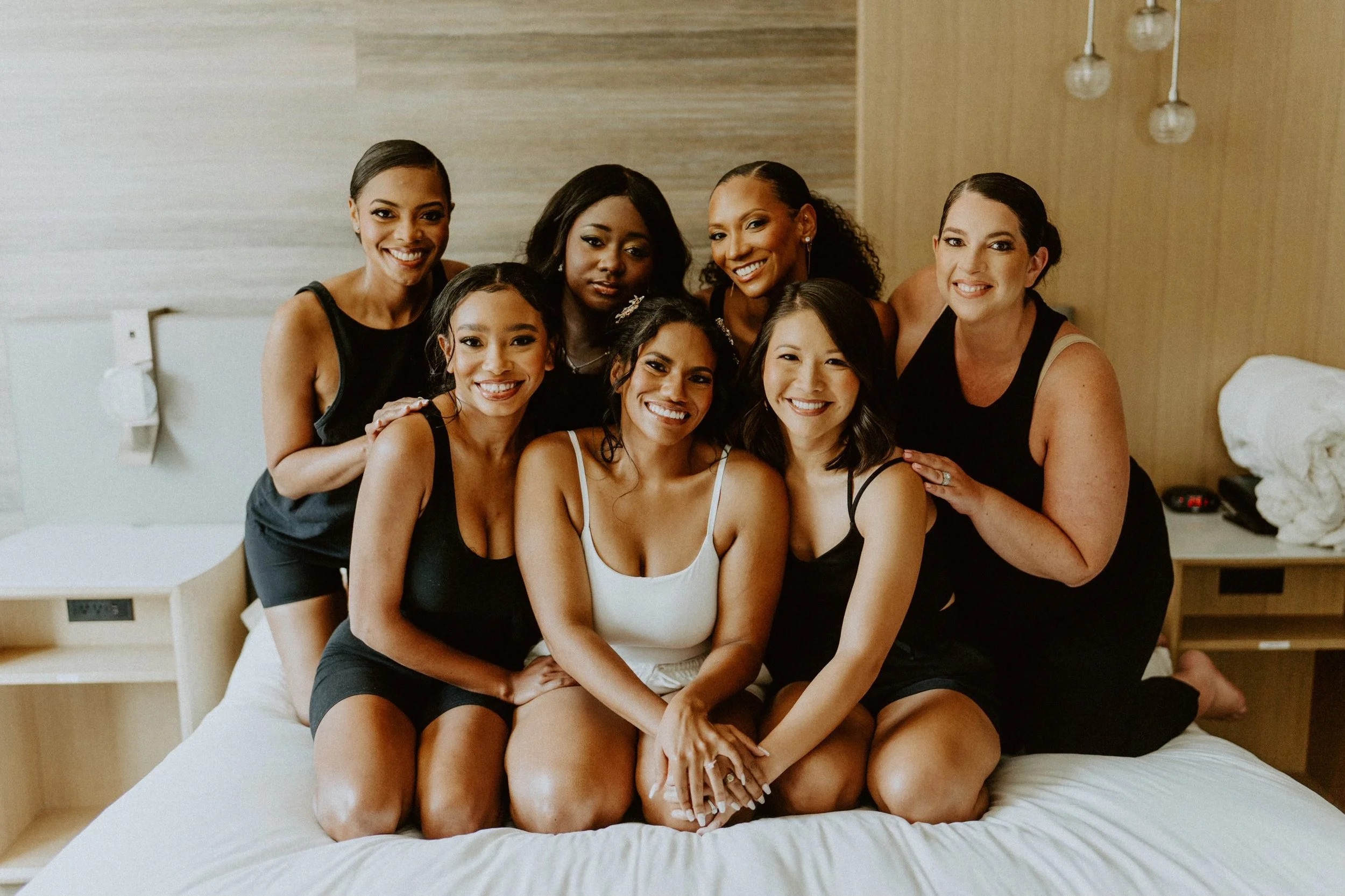 A Bridal party of a Group of women sitting on a bed and smiling.