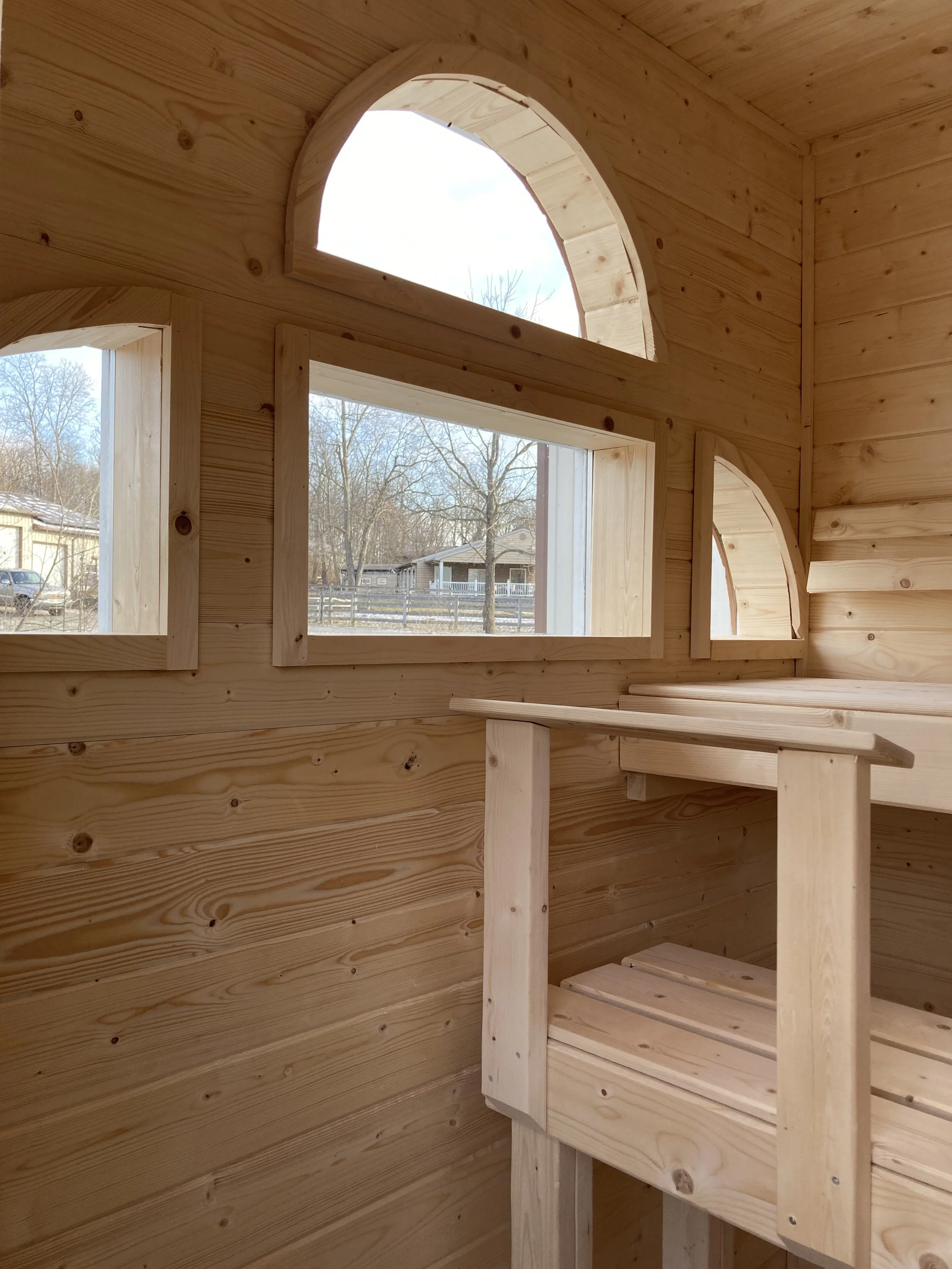 Spruce sauna interior with custom curved windows, ergonomic back rests, and foot rests