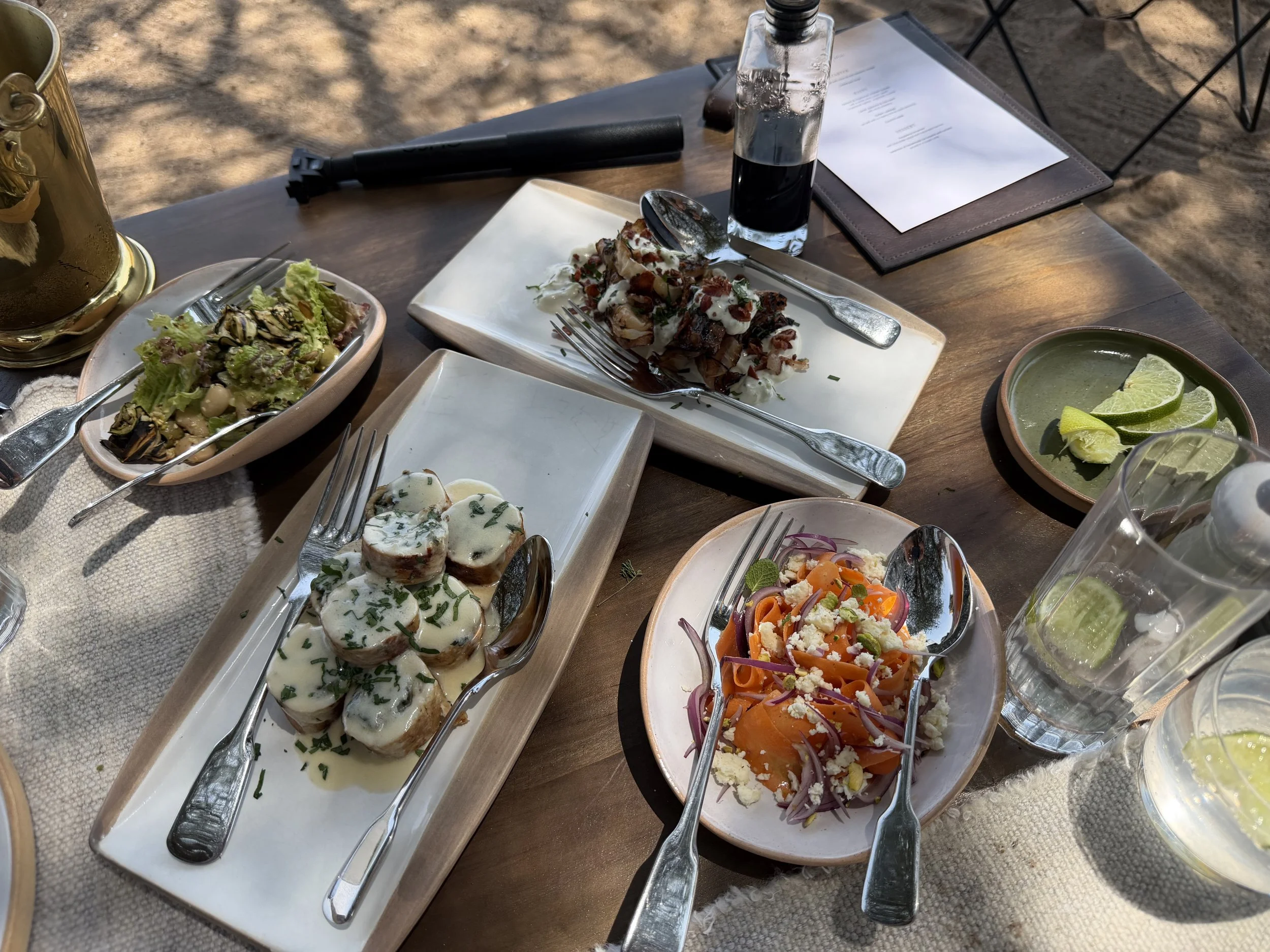 Lunch at Mila served as small plates, with salads and grilled dishes on a table set outdoors in the shade