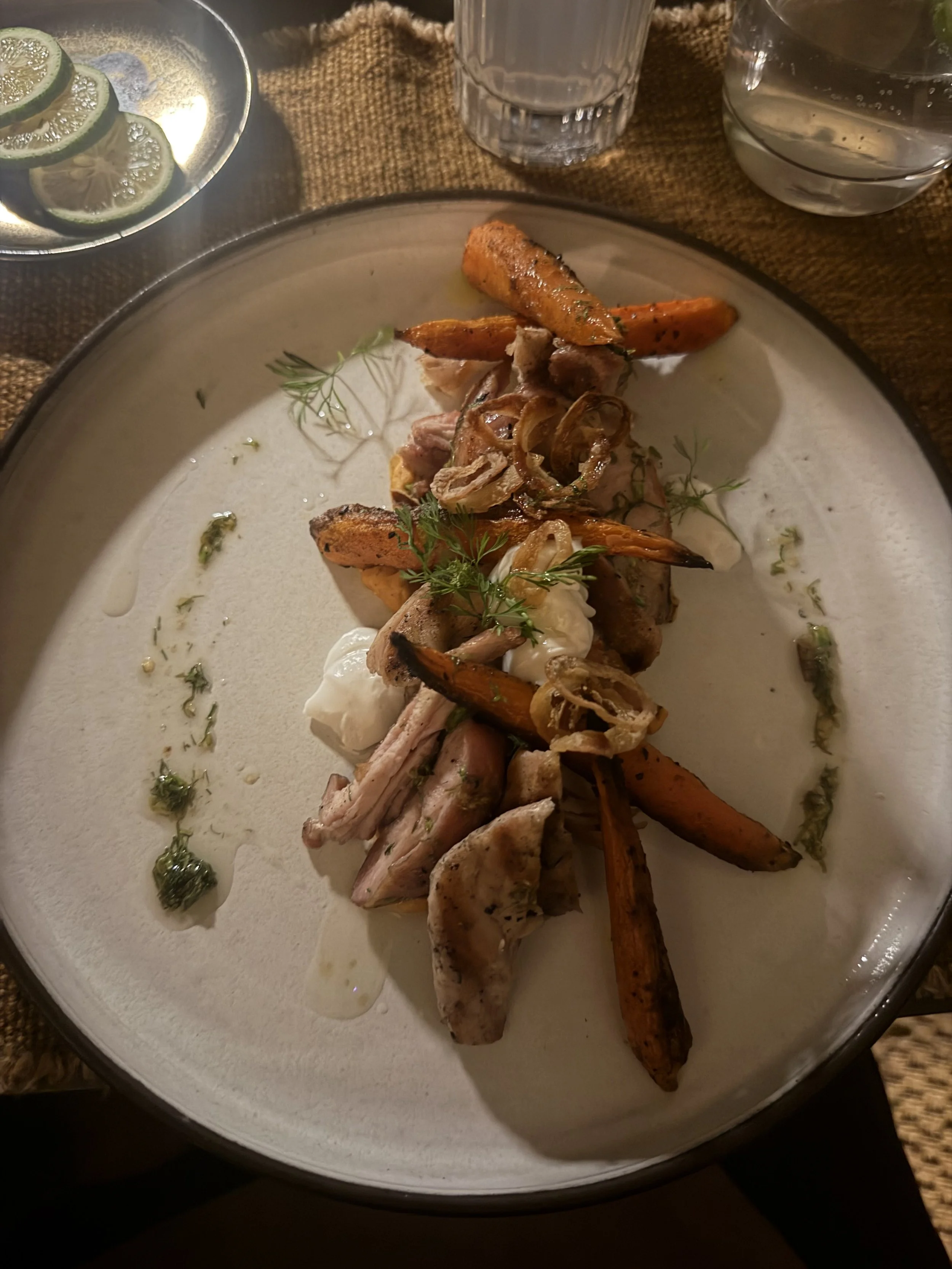 Plated dinner of chicken with roasted carrots and herb oil at Mila