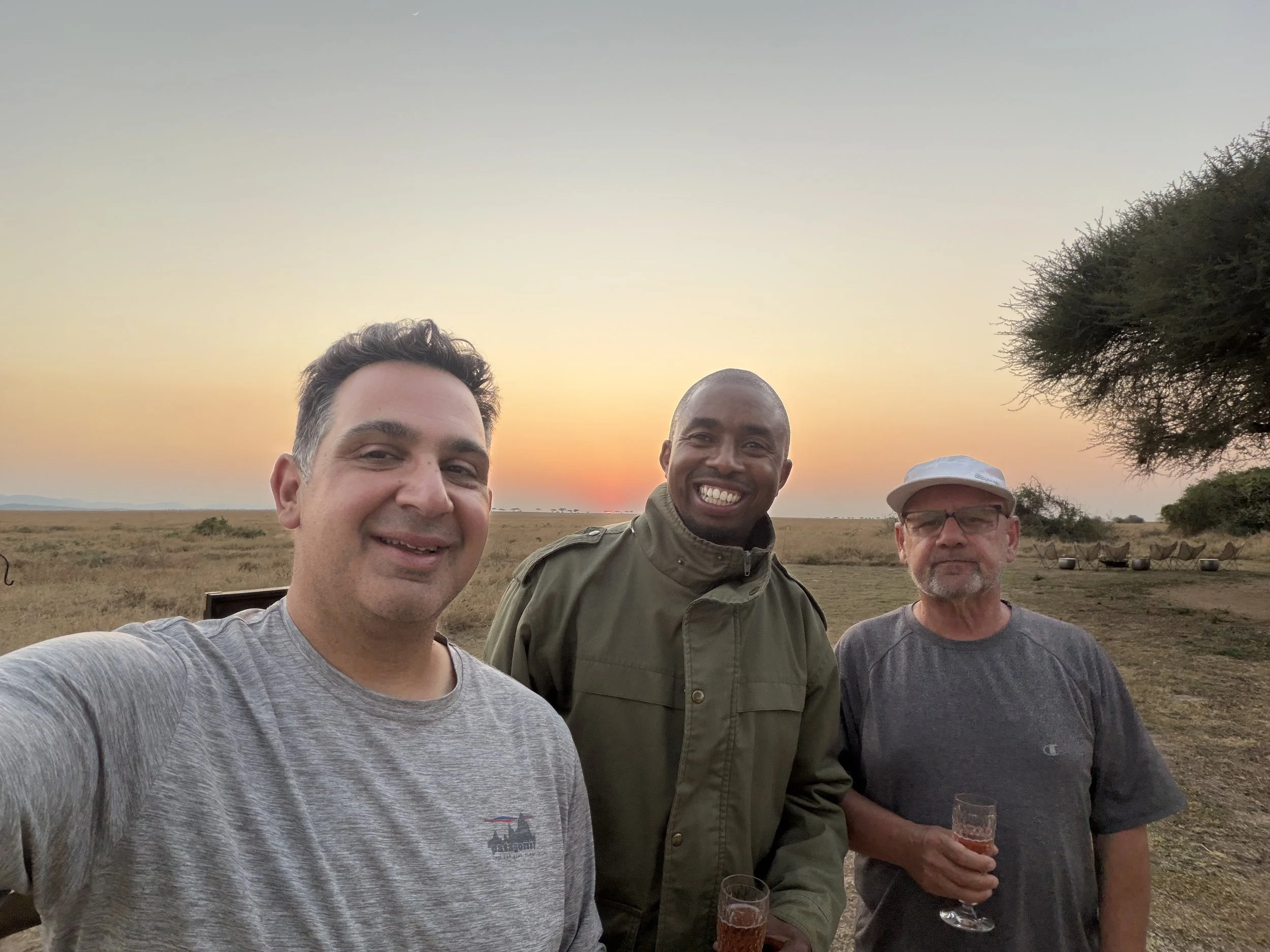 Three of us with drinks at sundowners on the open plains at sunset, near Mila in the Serengeti