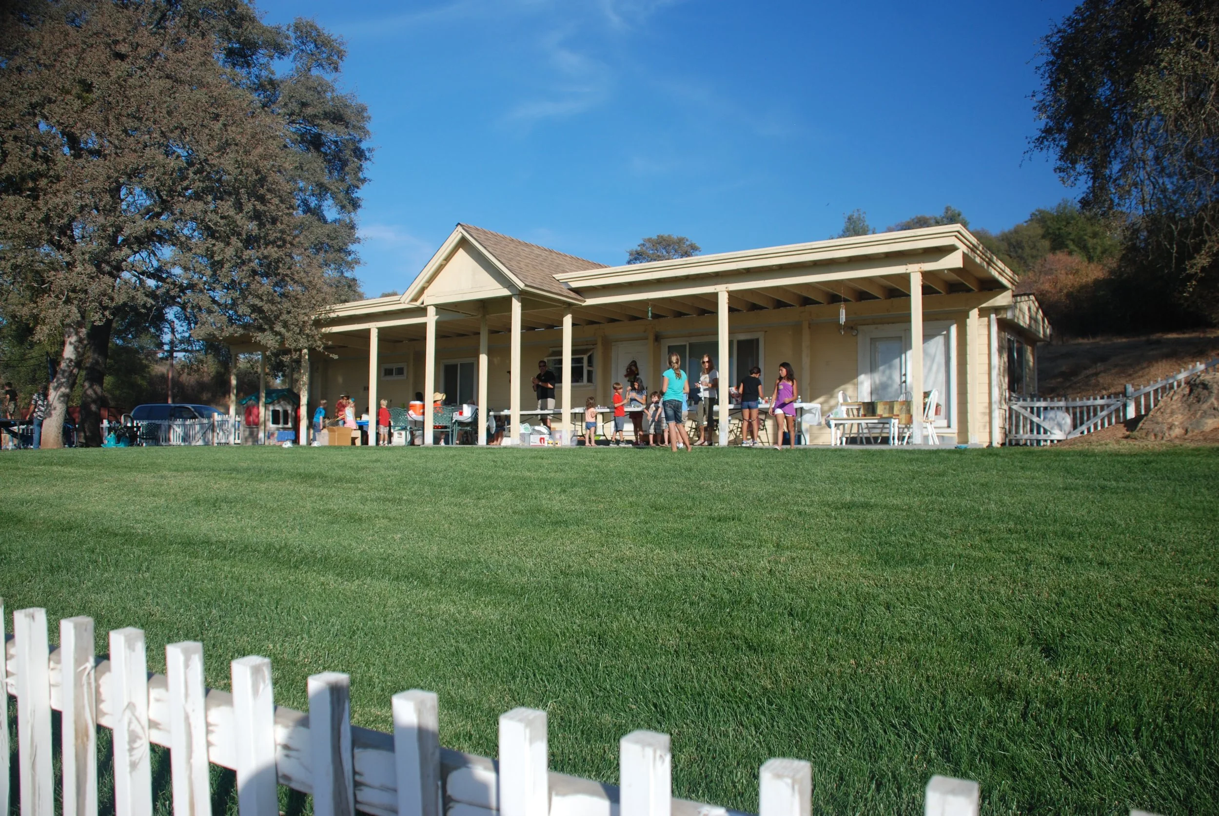 A birthday party at one of the small farmhouses in the Catholic Community found at Our Lady's Ranch. The house is a darling yellow surrounded by a white picket fence under a blue sky.