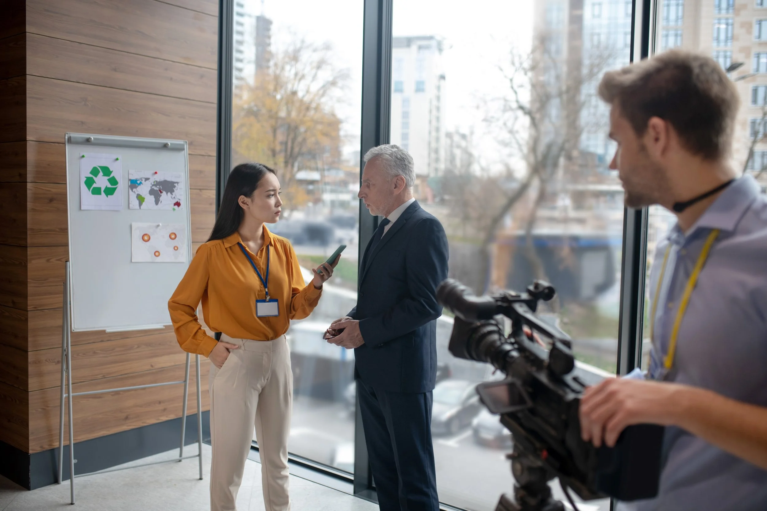 A female reporter wearing business casual attire and speaking to a professional man in a suit.