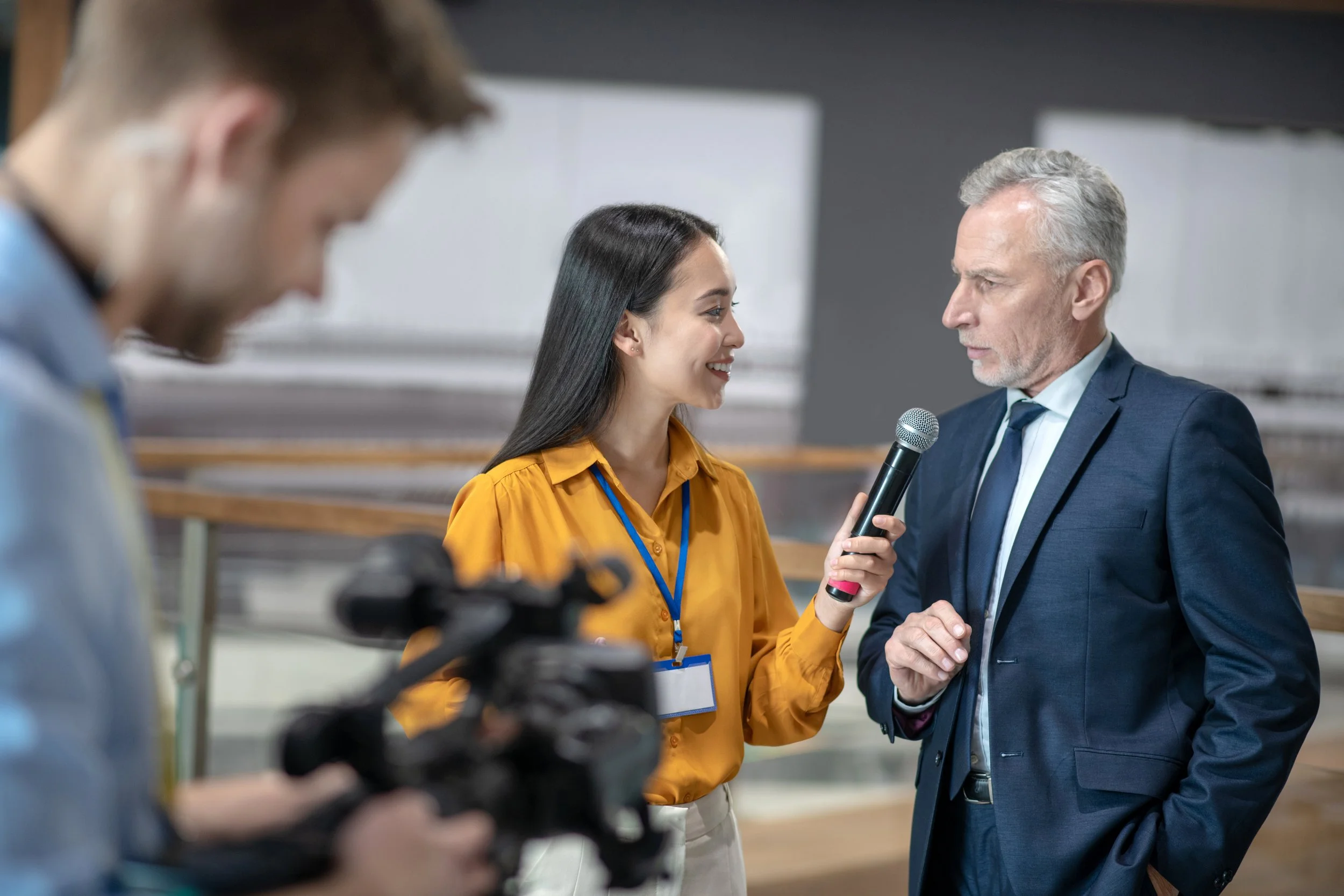 A young reporter interviewing a man in a suit while a cameraman records the interaction.