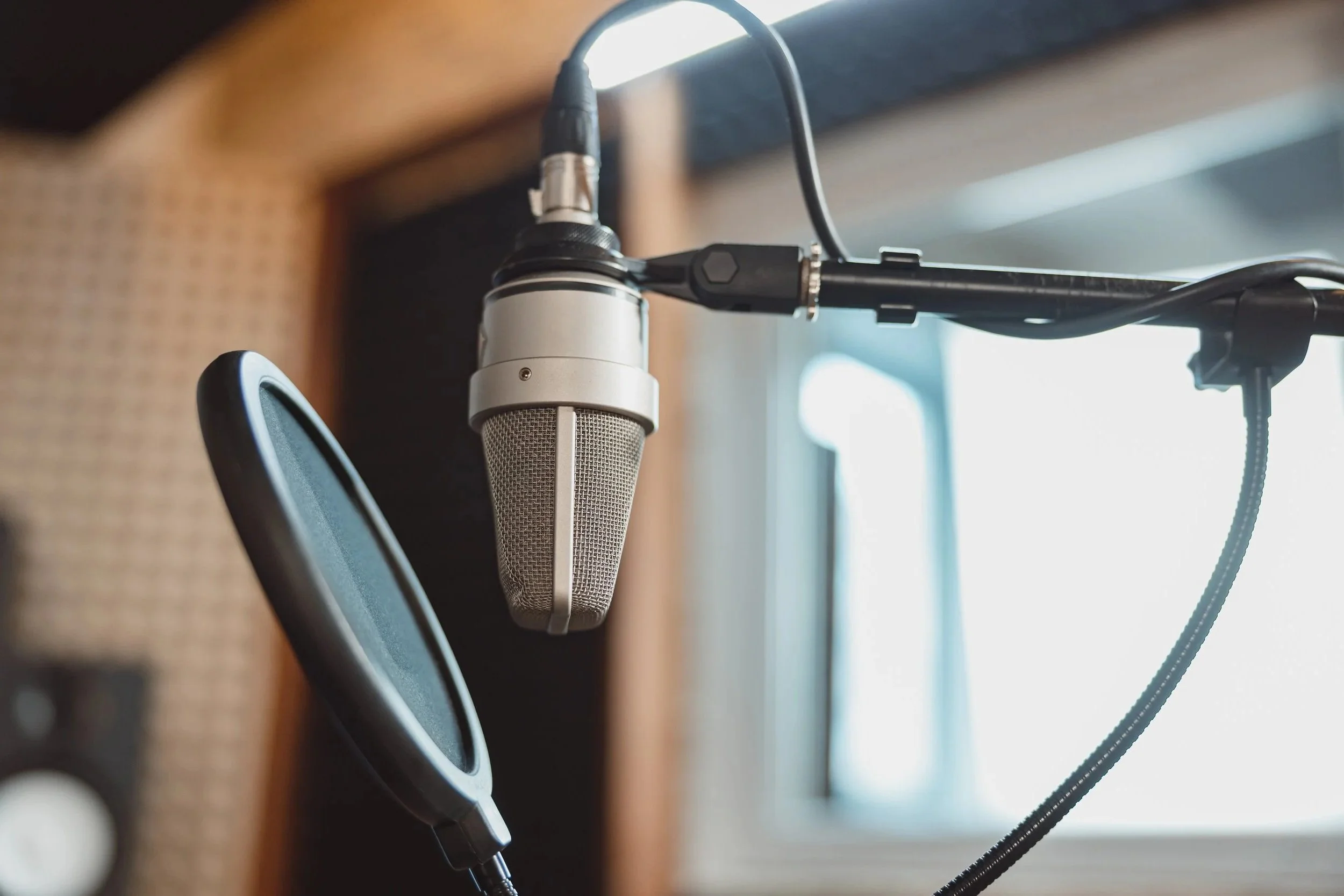 Close-up of a studio microphone with a pop filter hanging in front of it, in a recording studio with soundproof walls.