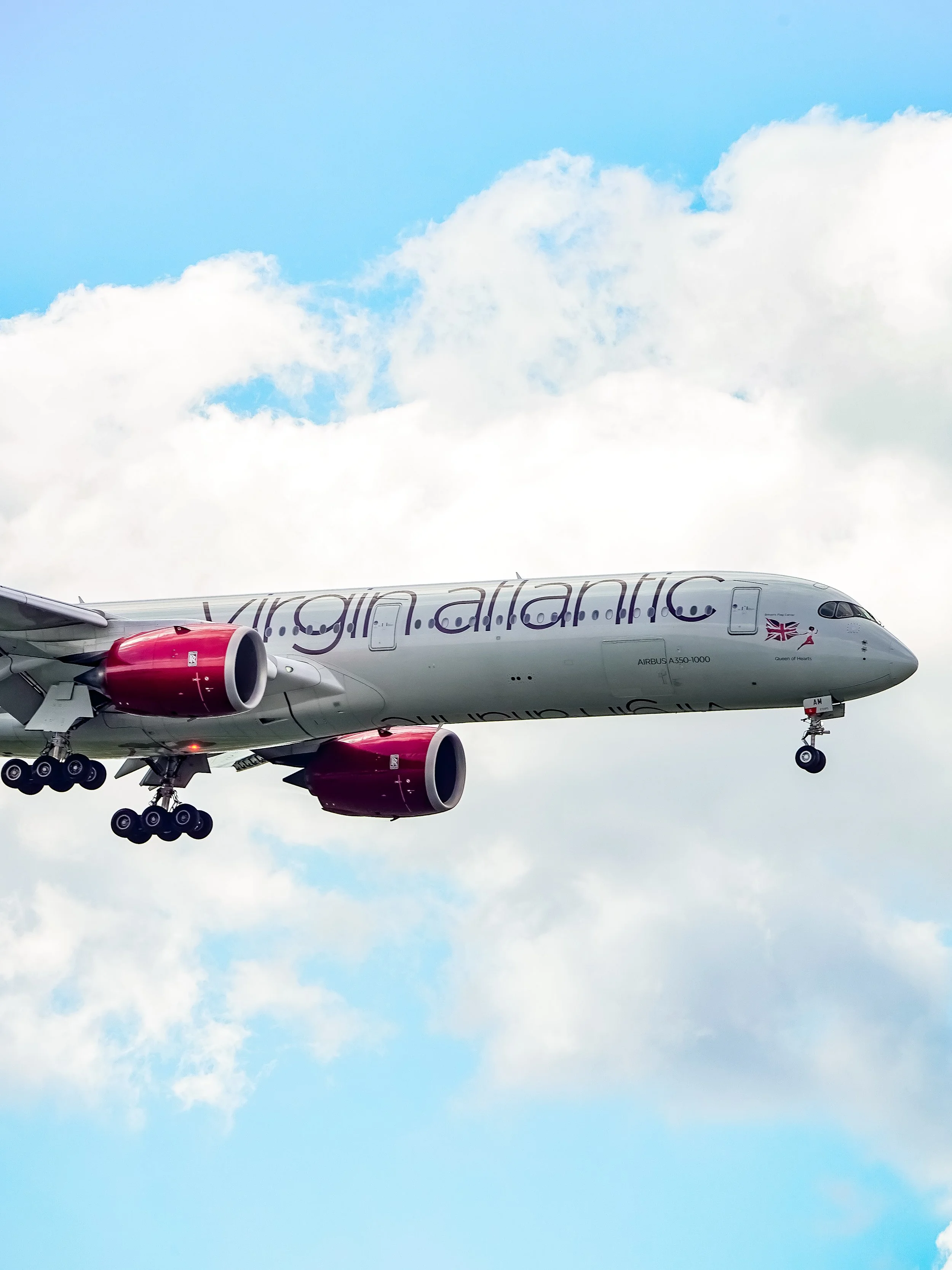 Virgin Atlantic airplane flying in the sky with clouds in the background.