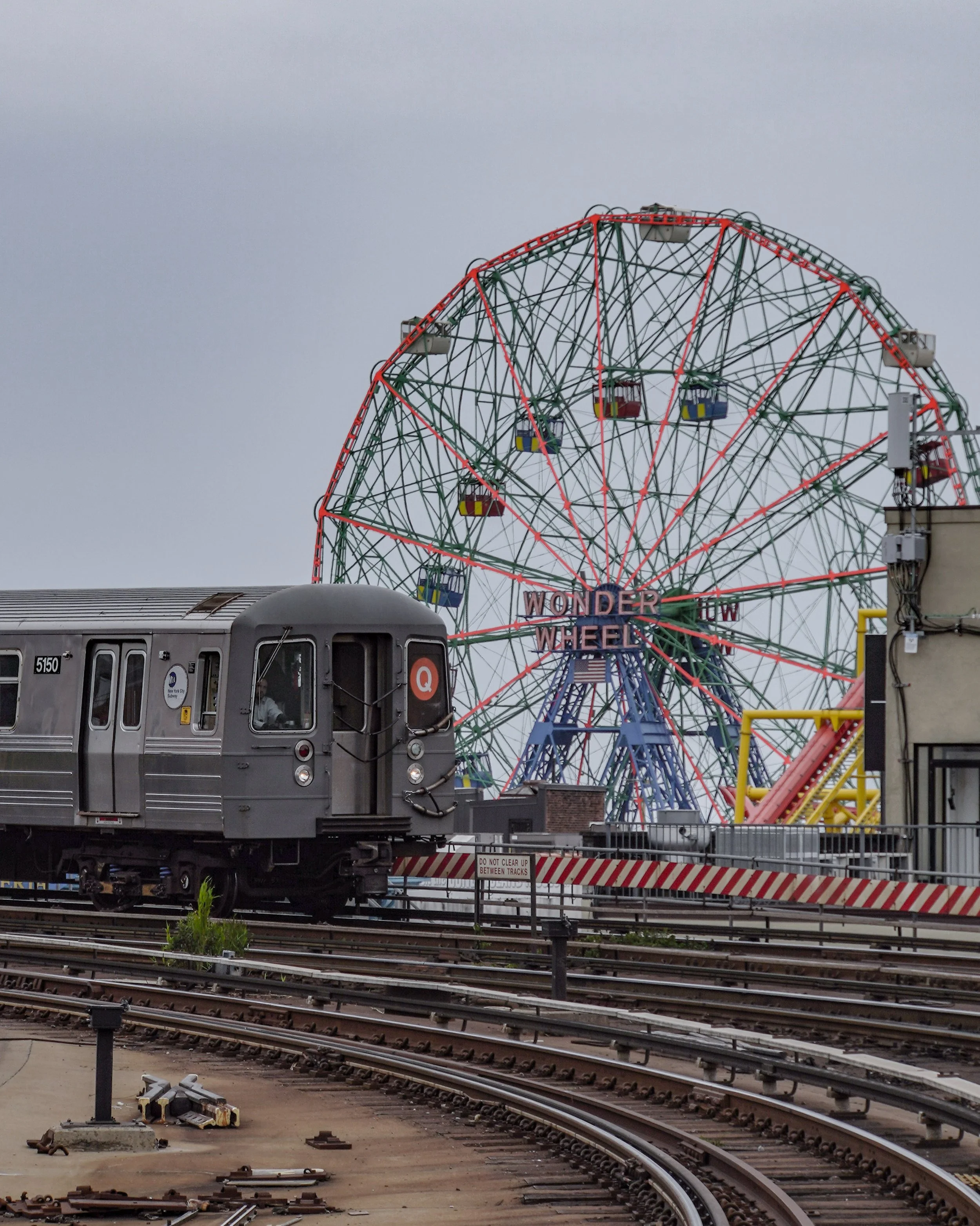A grey subway train on tracks in front of a colorful Ferris wheel labeled 'Wonder Wheel' at an amusement park.
