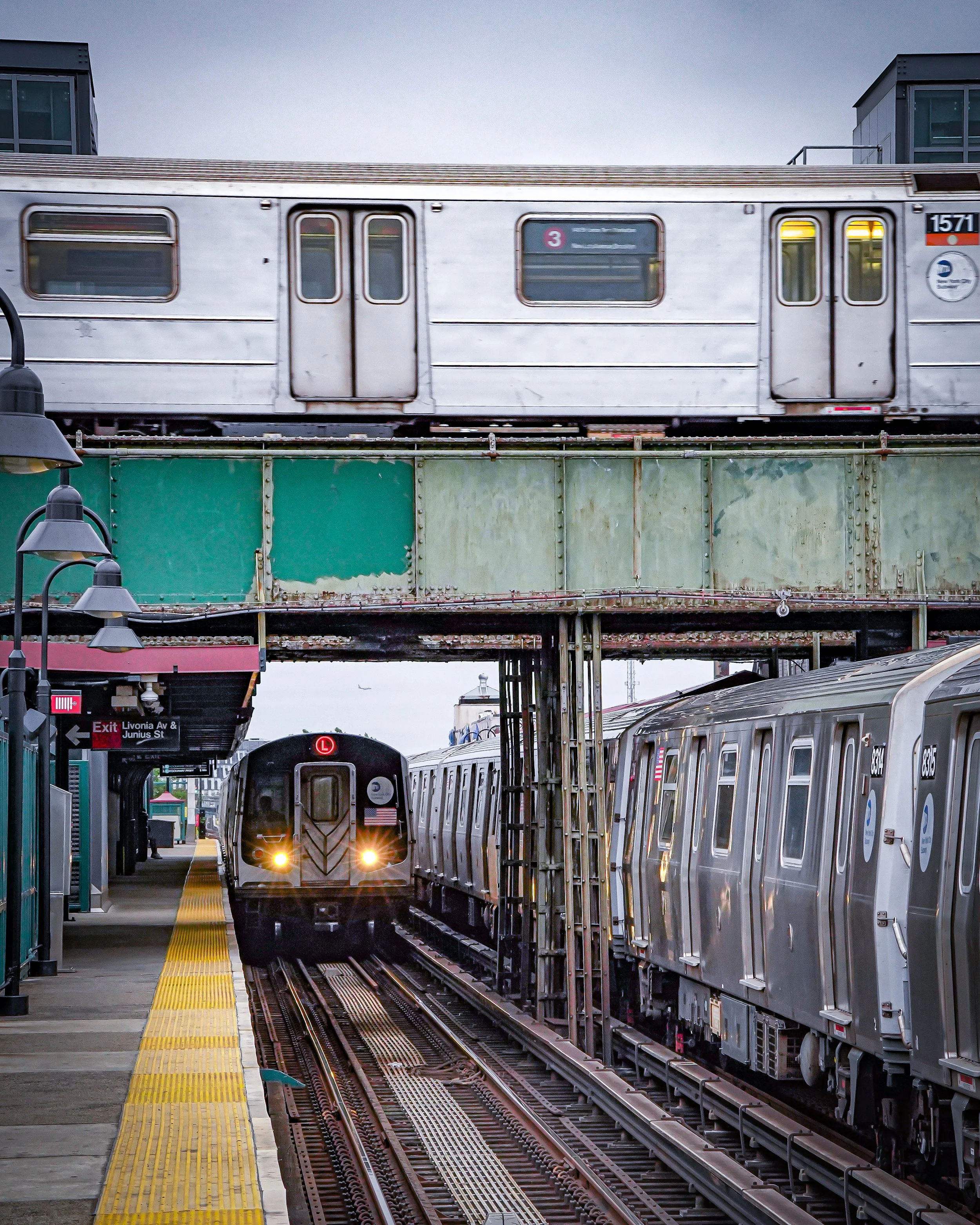 Subway trains on elevated tracks above a subway station platform with a train approaching on the tracks below.