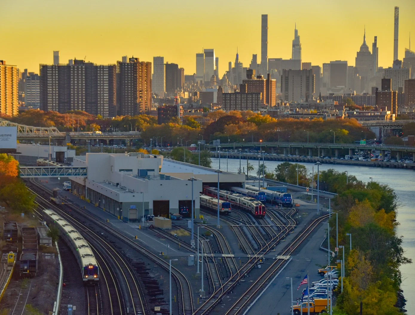 New York City skyline withtrain tracks in the foreground and a river along the side at sunset.