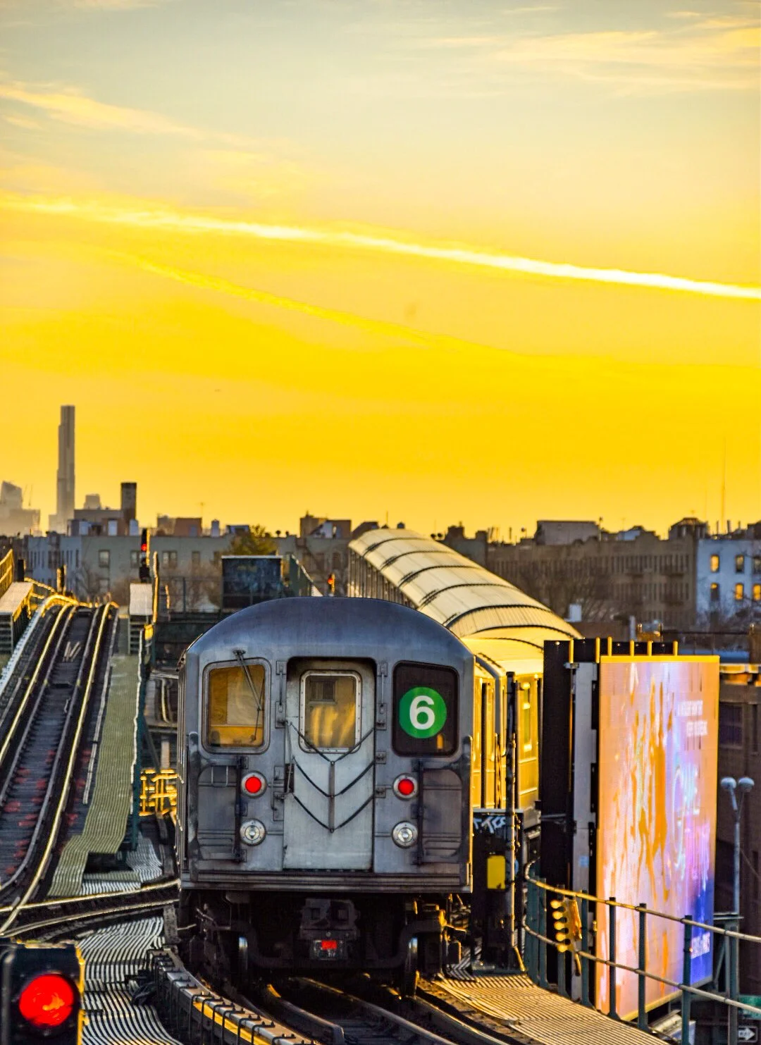 A train on elevated tracks during sunset with a city skyline in the background.