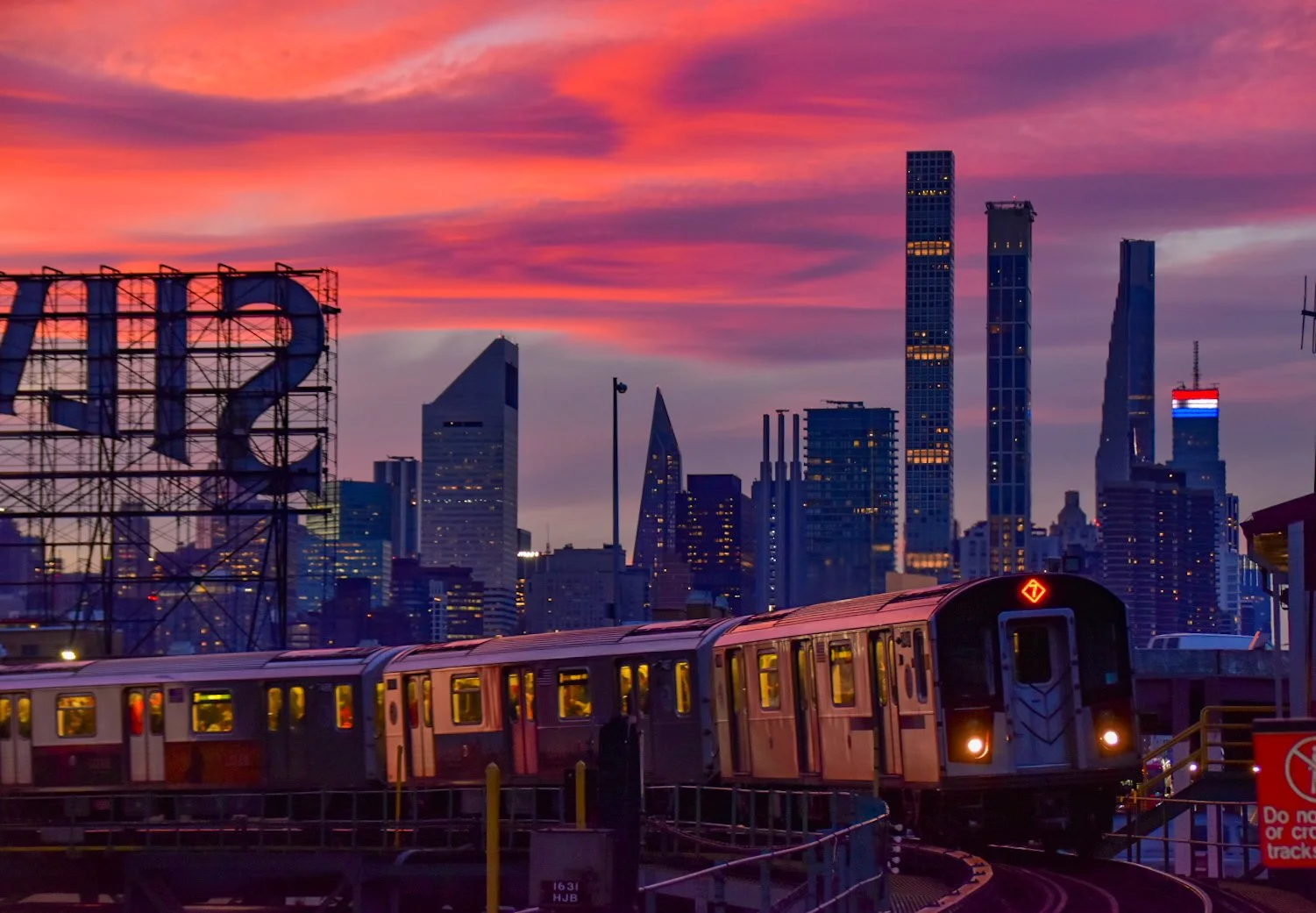 City skyline during a cotton candy sunset with skyscrapers and a train on elevated tracks in the foreground.
