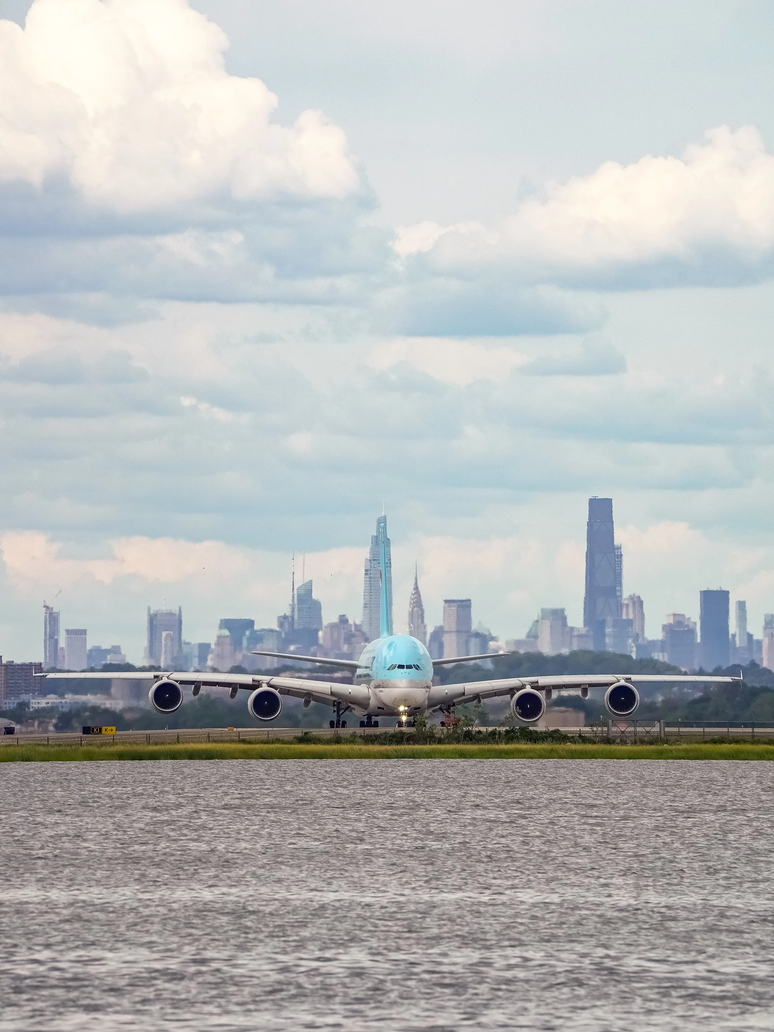A large commercial airplane on runway with city skyline in background, cloudy sky.