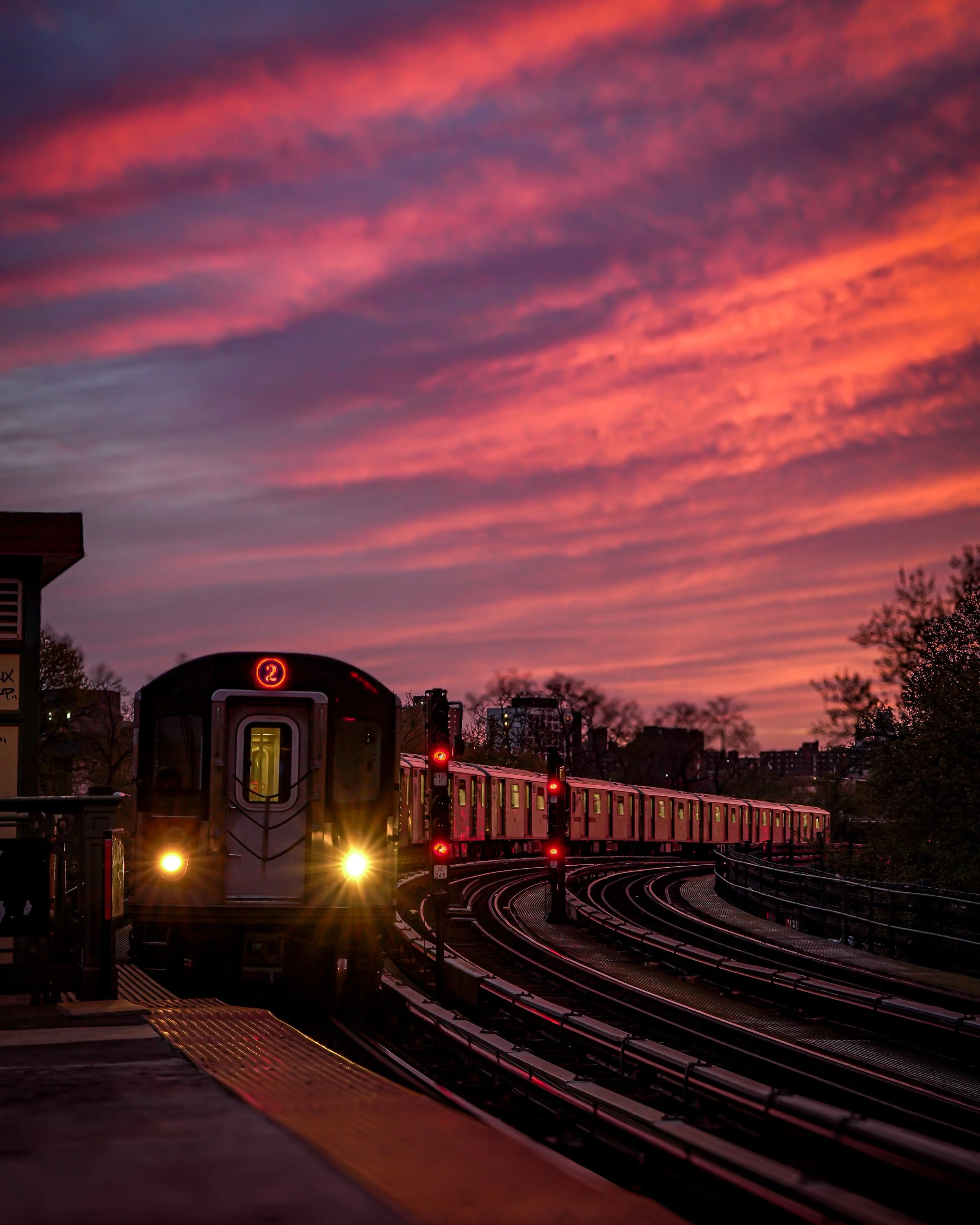 A train arriving at a station with a colorful sunset sky in the background.