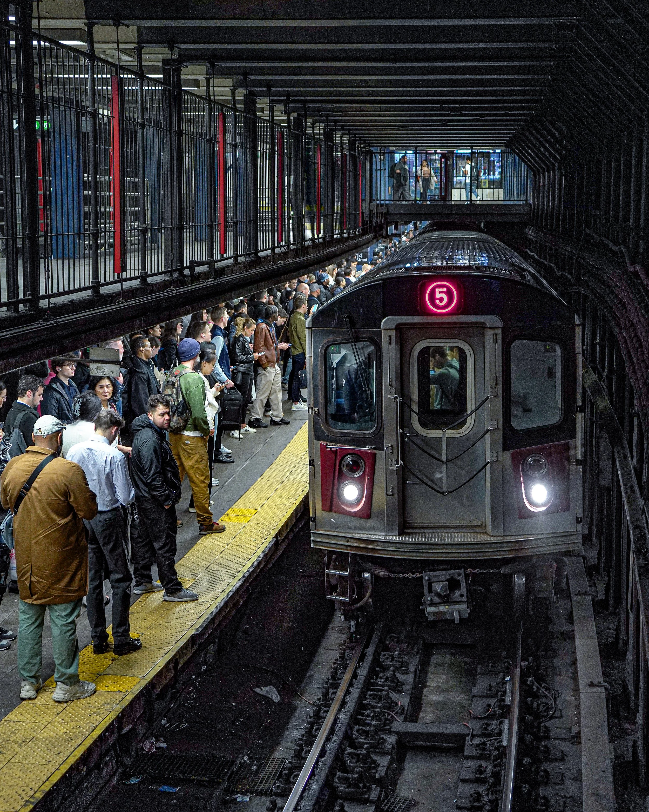 Subway train arriving at underground station with passengers waiting on platform.