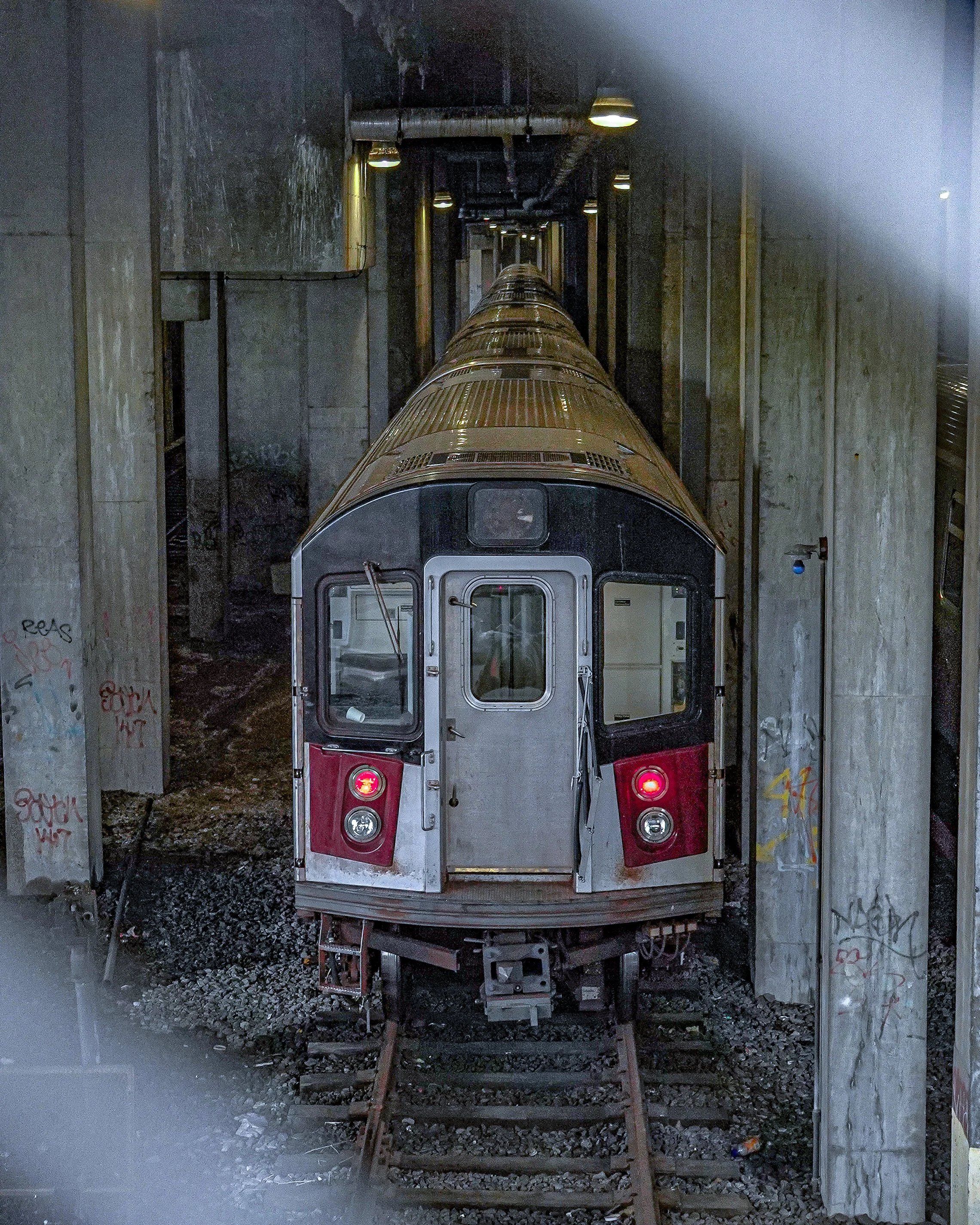 A subway train moving through a tunnel beneath a city street, illuminated by overhead lights.