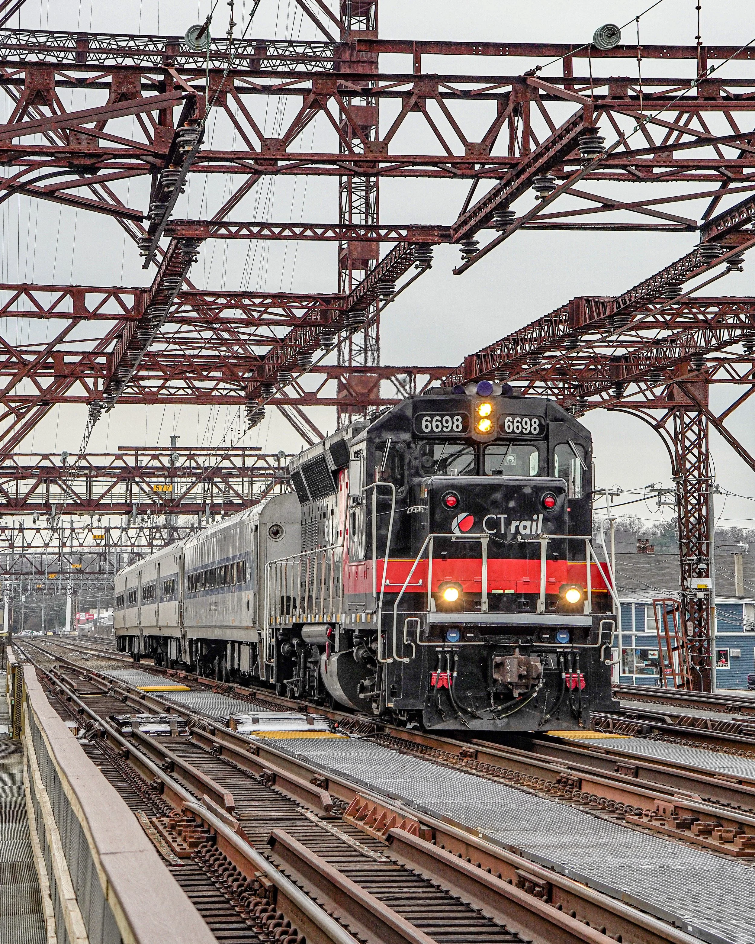 A CT Rail diesel locomotive train moving on tracks under a network of overhead electrical wires.
