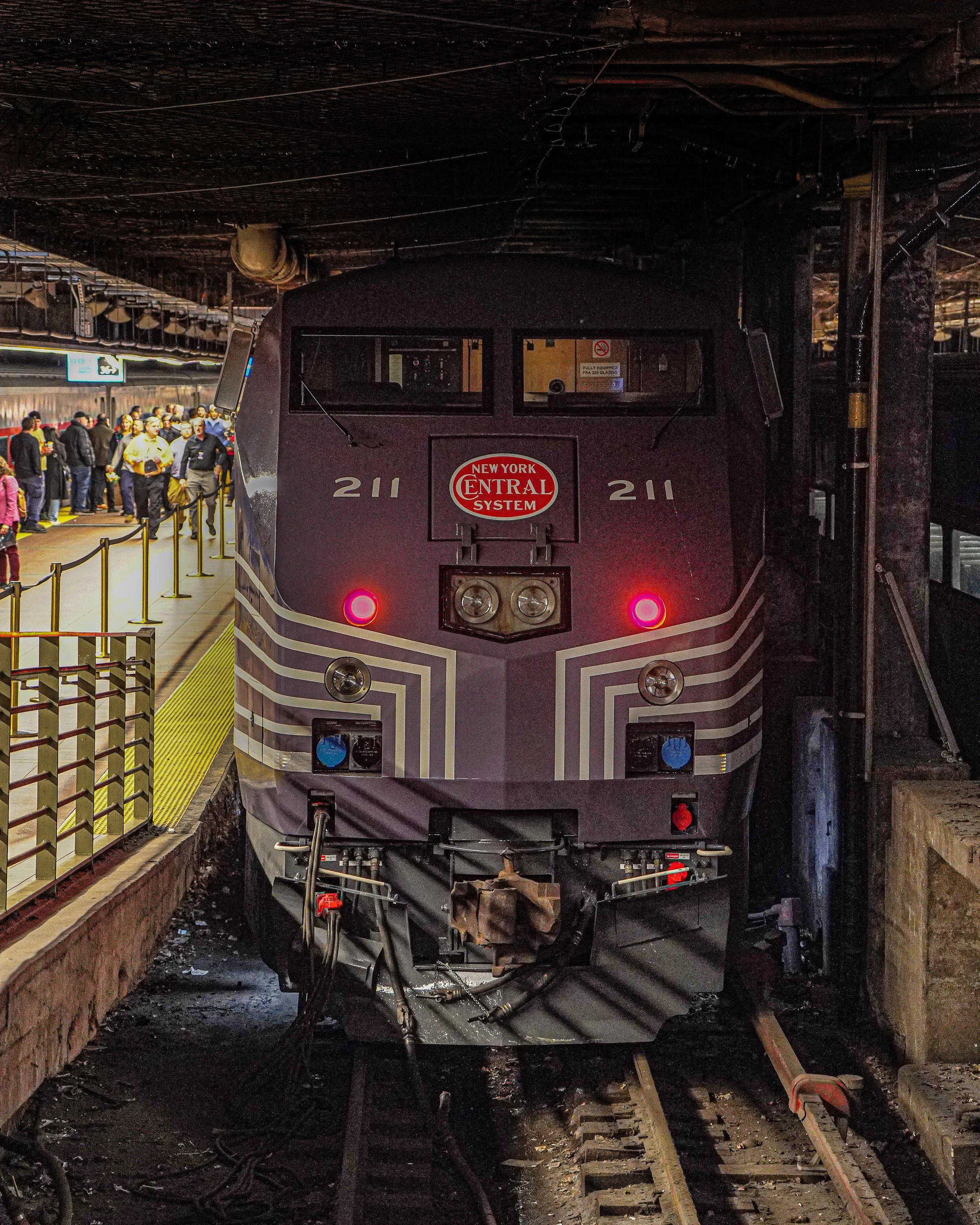 Front view of New York Central Metro-North diesel train inside a station with a crowd of people on the platform to the left.