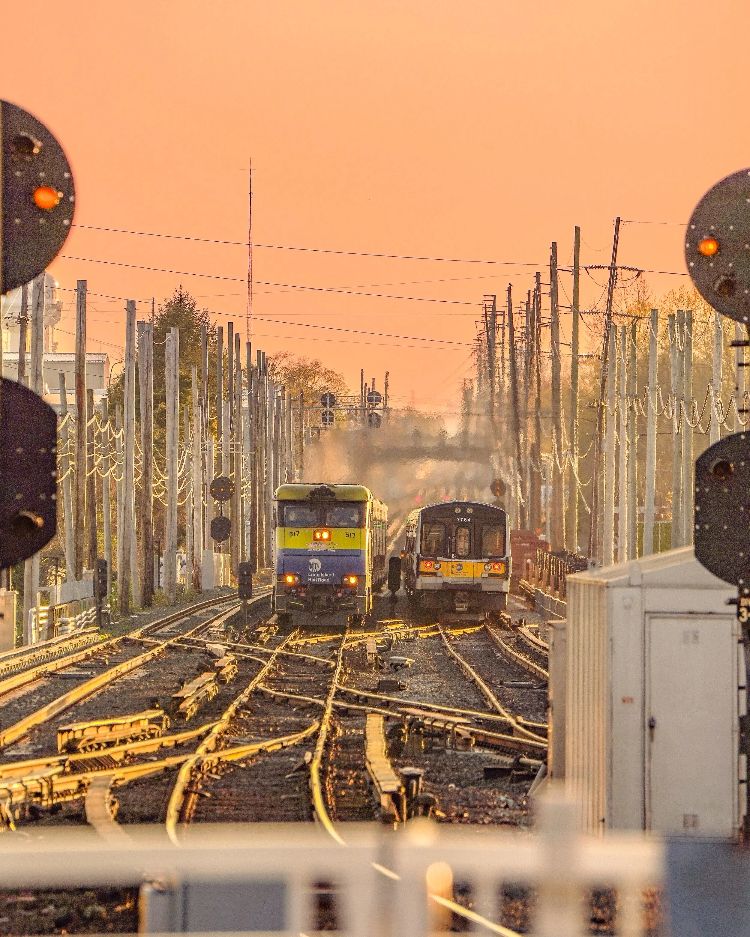 Two trains on parallel tracks at sunset, with multiple railway signals and utility poles along the tracks.