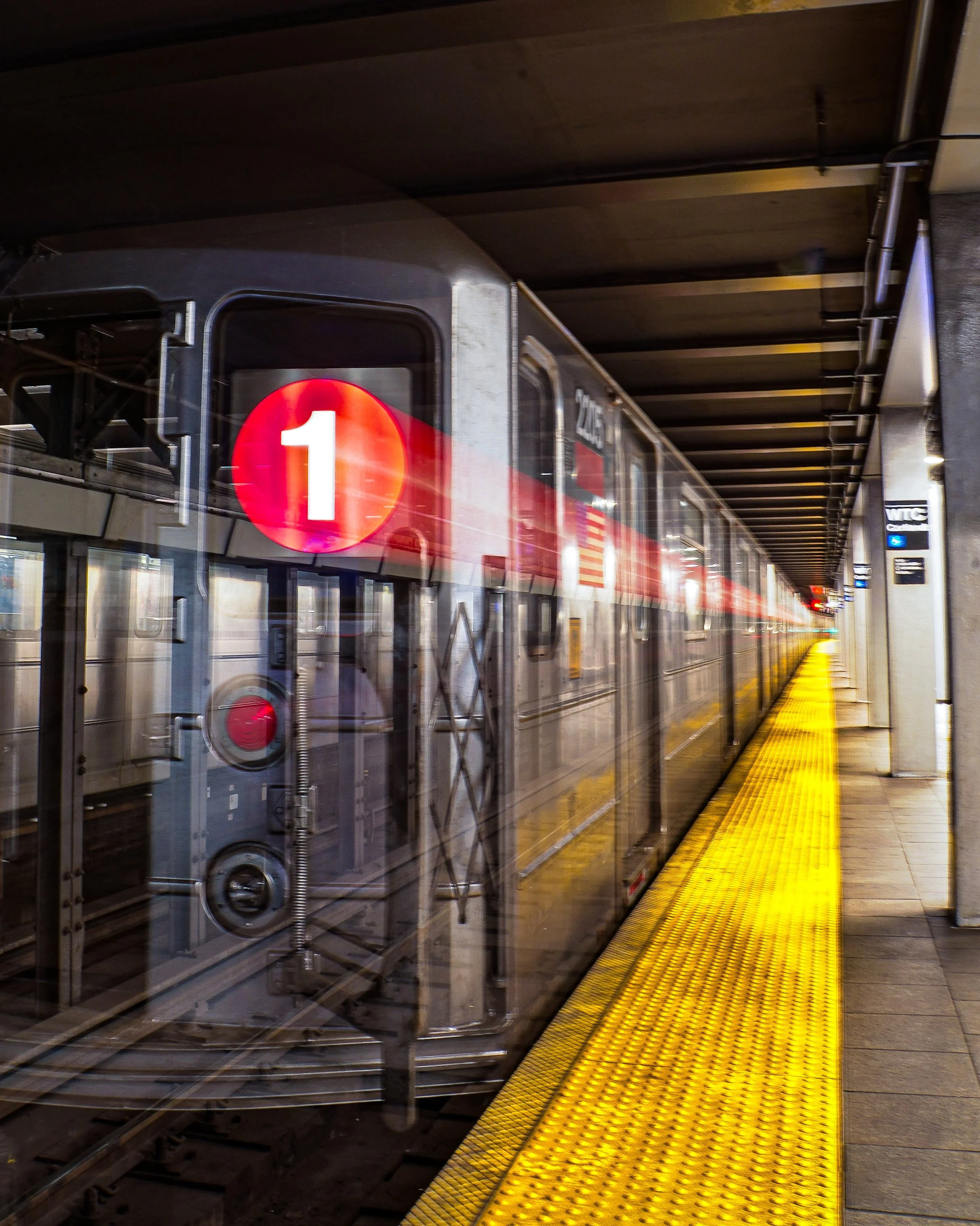 A 1 subway long exposure ghost train departing at an underground station, viewed through a glass reflection, with a yellow tactile paving strip along the platform edge.