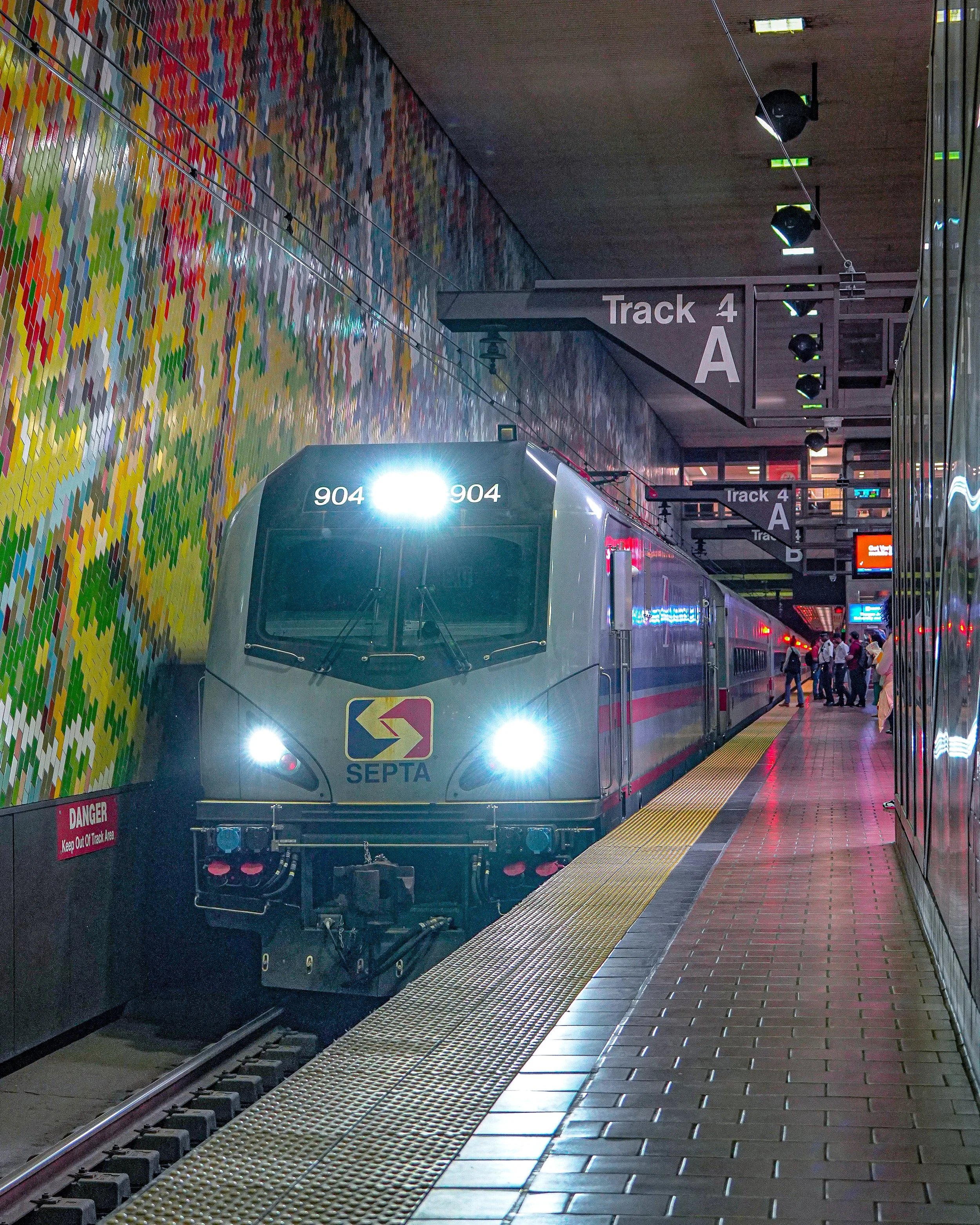 A SEPTA train arriving at an underground station, with colorful mosaic wall art on the left and signs indicating Track 4 A.