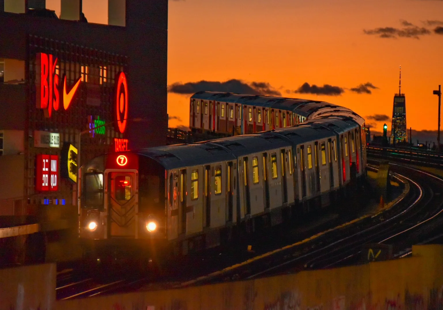 A train on an elevated track during sunset with a city skyline in the background.