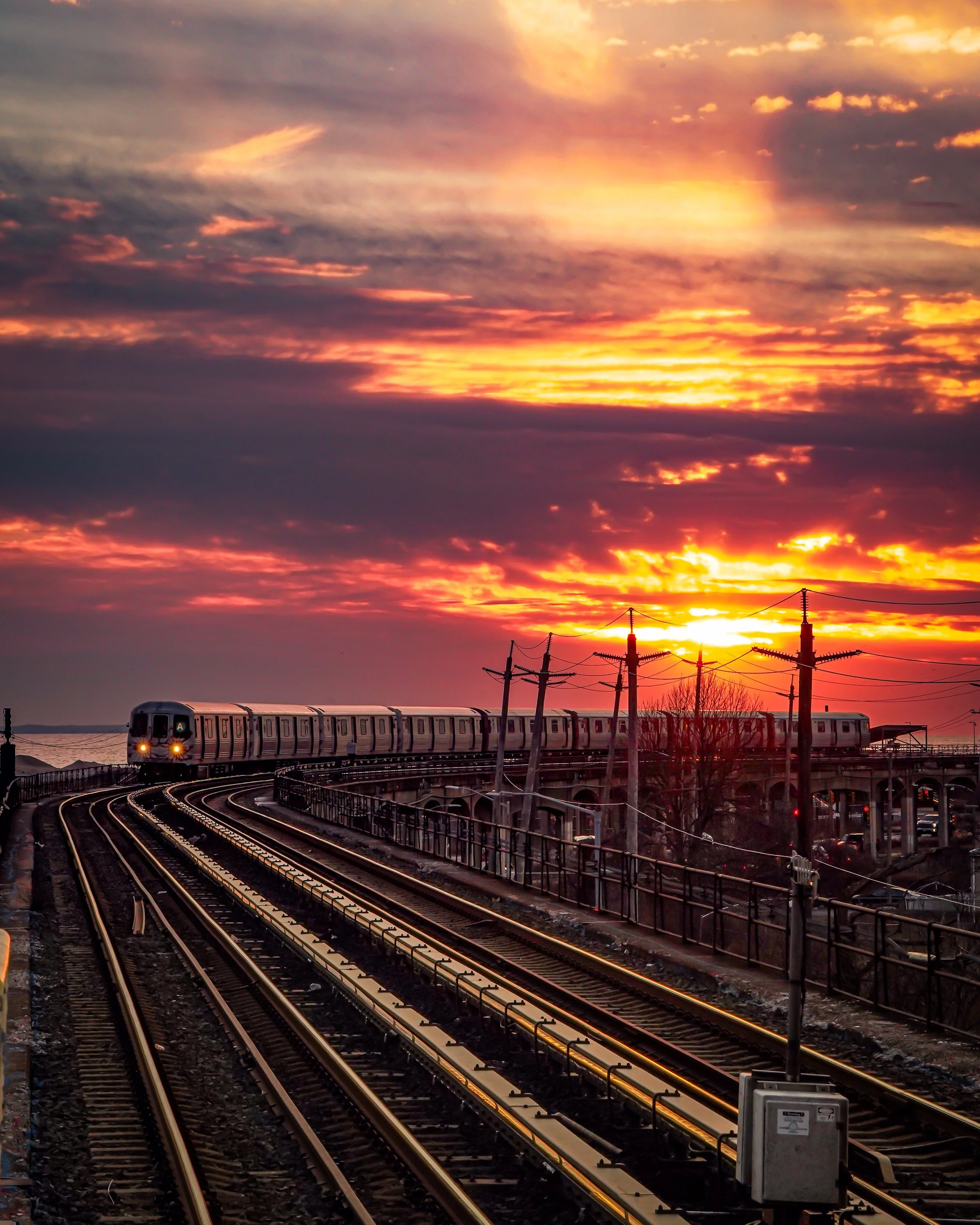 A train on elevated tracks during a vibrant sunset with colorful clouds in the sky.