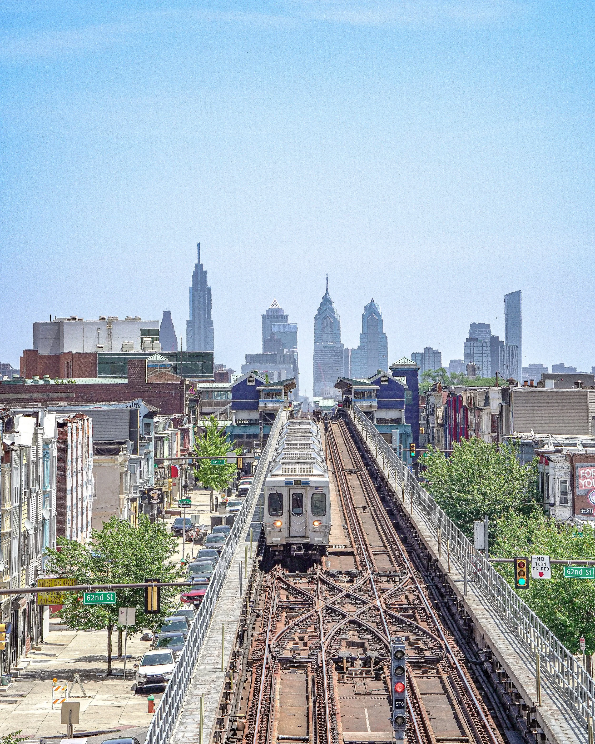 An elevated train on the tracks of a city rail system with the Philadelphia skyline in the background.