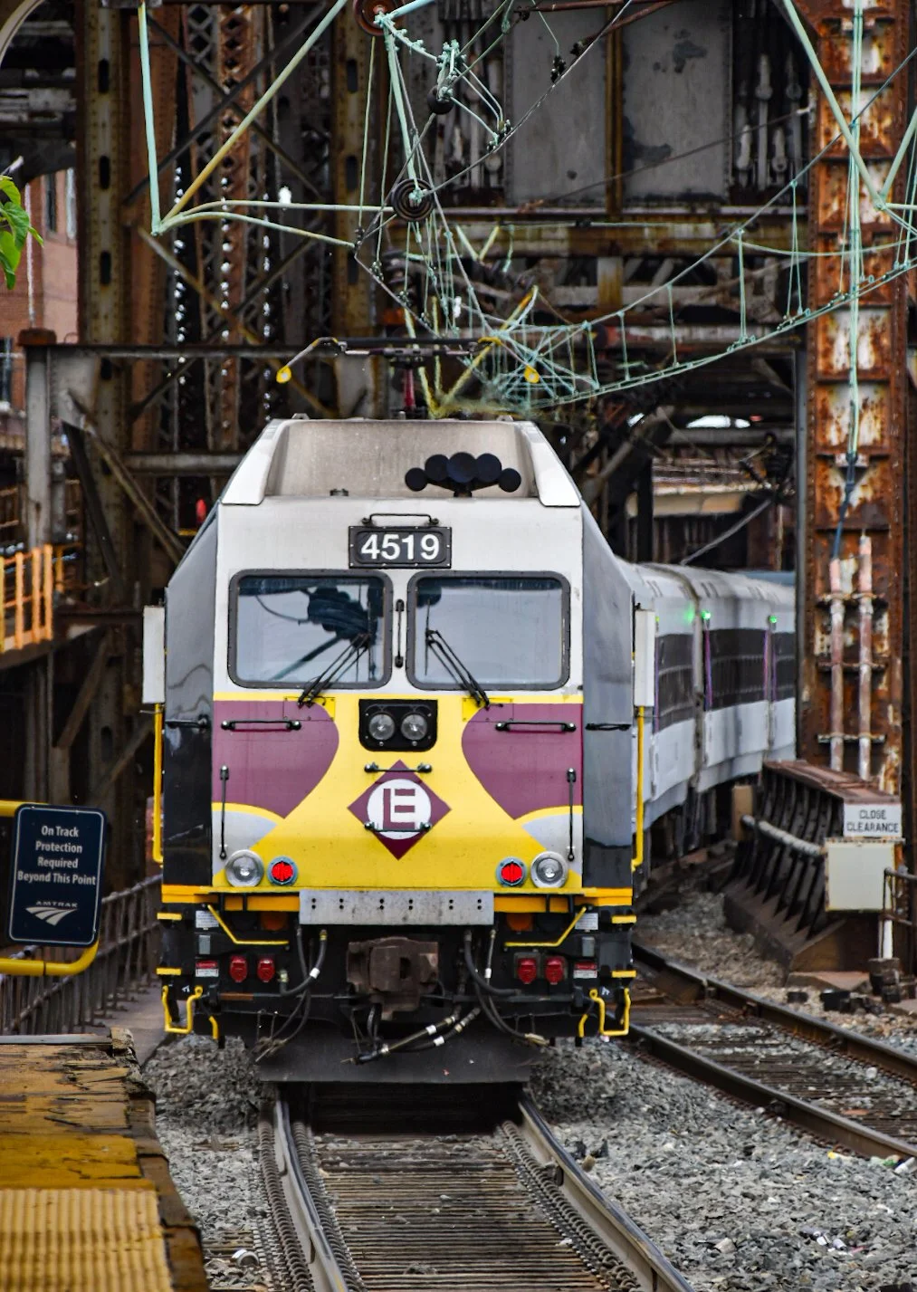 Front view of a yellow and white electric train with the number 4519, moving forward on railroad tracks through an urban industrial environment.