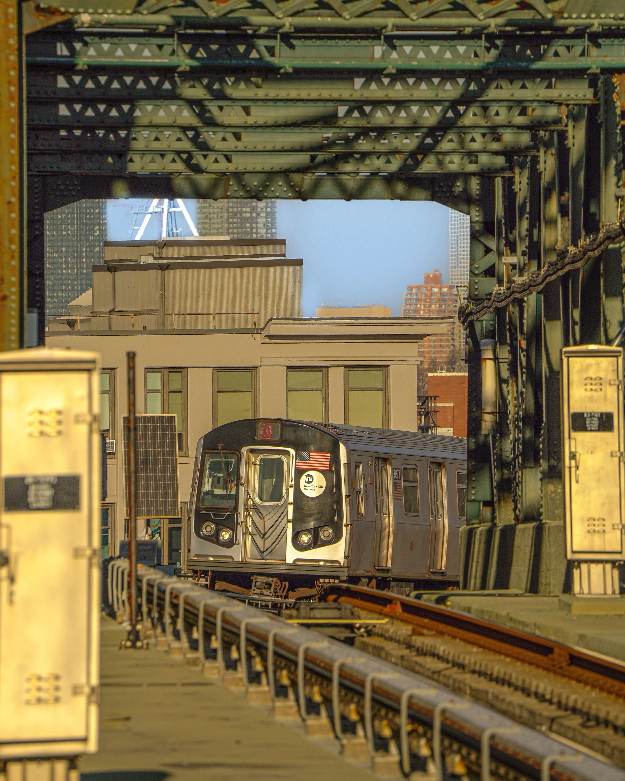 Subway train on elevated track in New York City with buildings in the background.