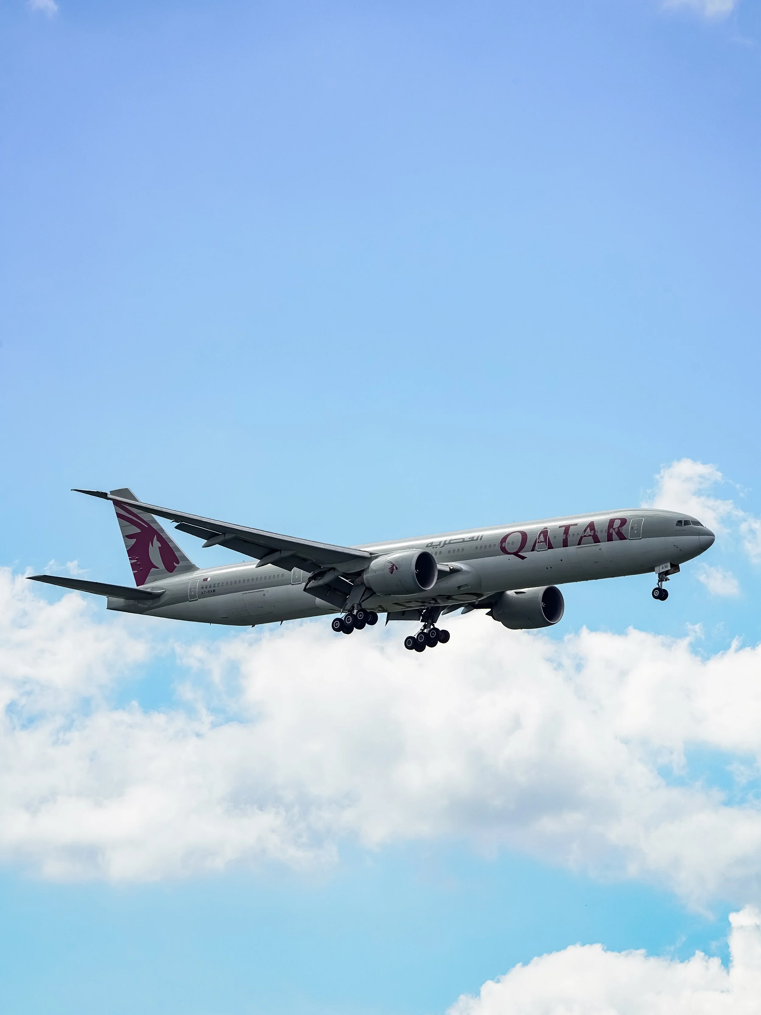 A Qatar Airways airplane flying in a partly cloudy sky.
