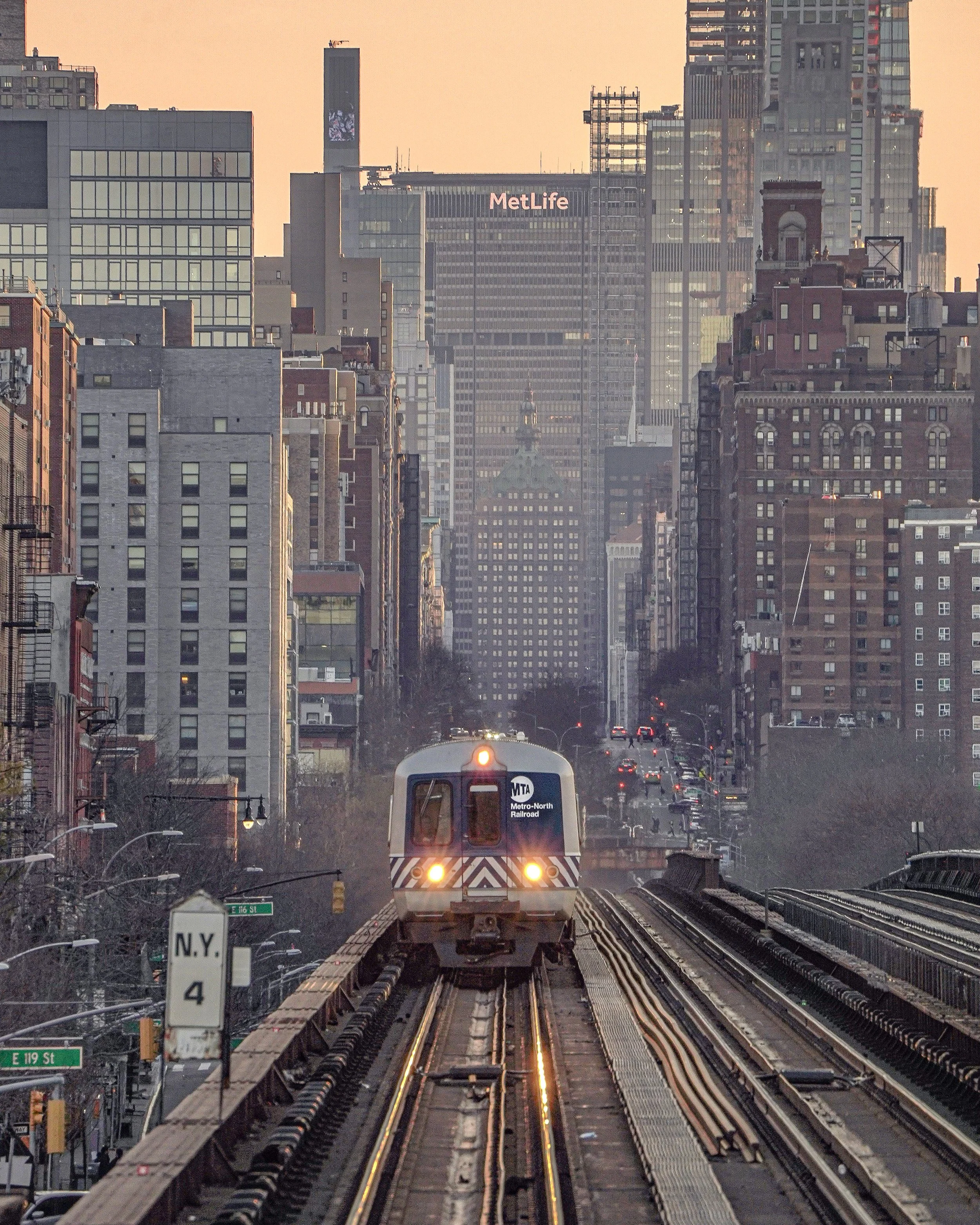 A subway train traveling on elevated tracks through New York City with tall buildings and skyscrapers in the background.