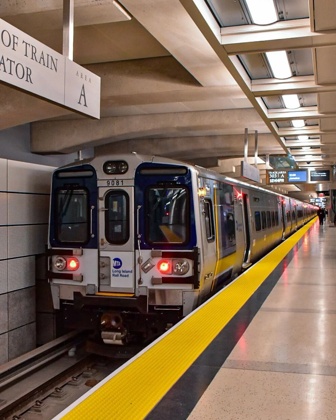 NYC subway train at underground station with yellow safety line and digital signs overhead.