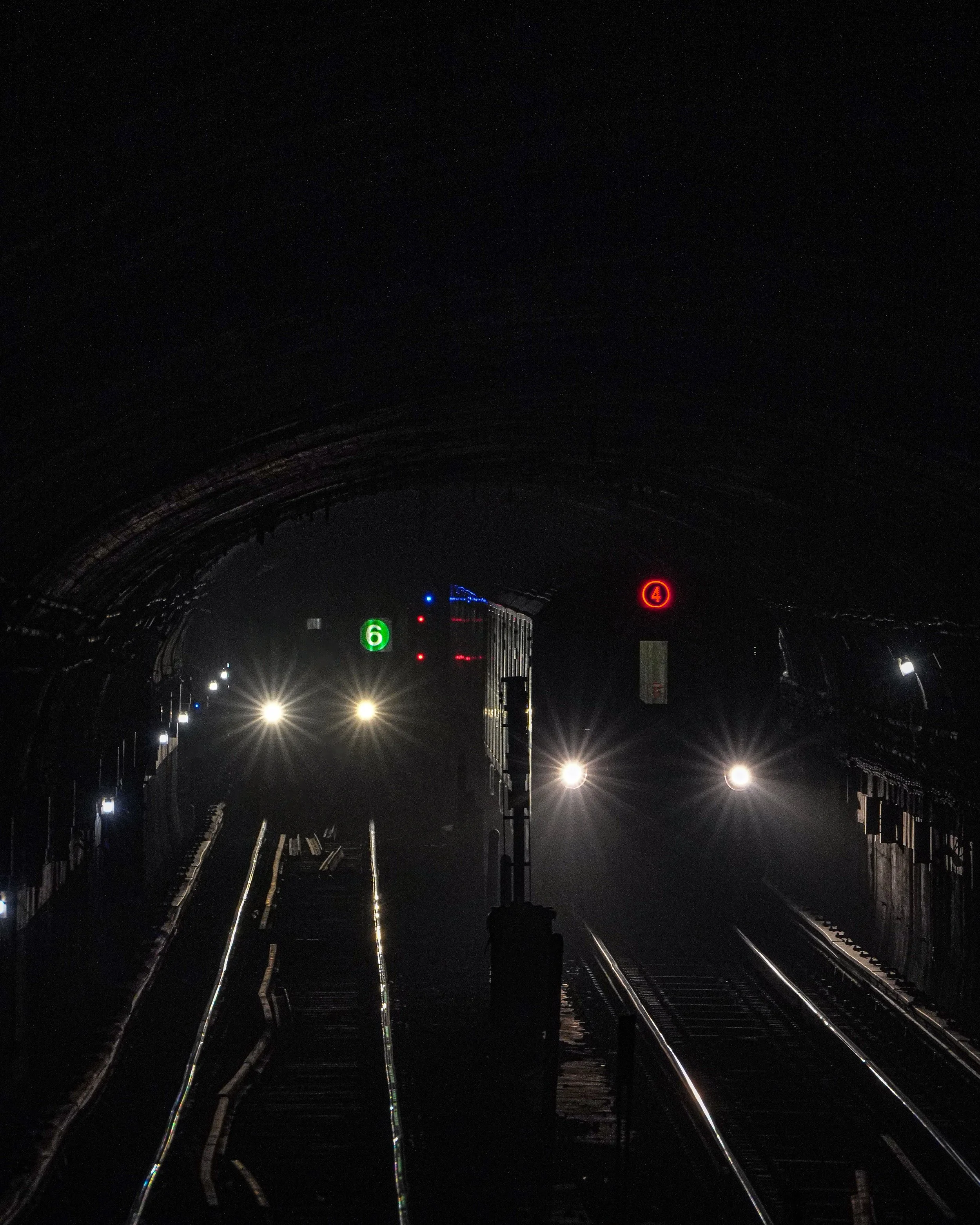 Dark subway tunnel with illuminated train headlights and digital signs displaying the numbers 6 and 4.